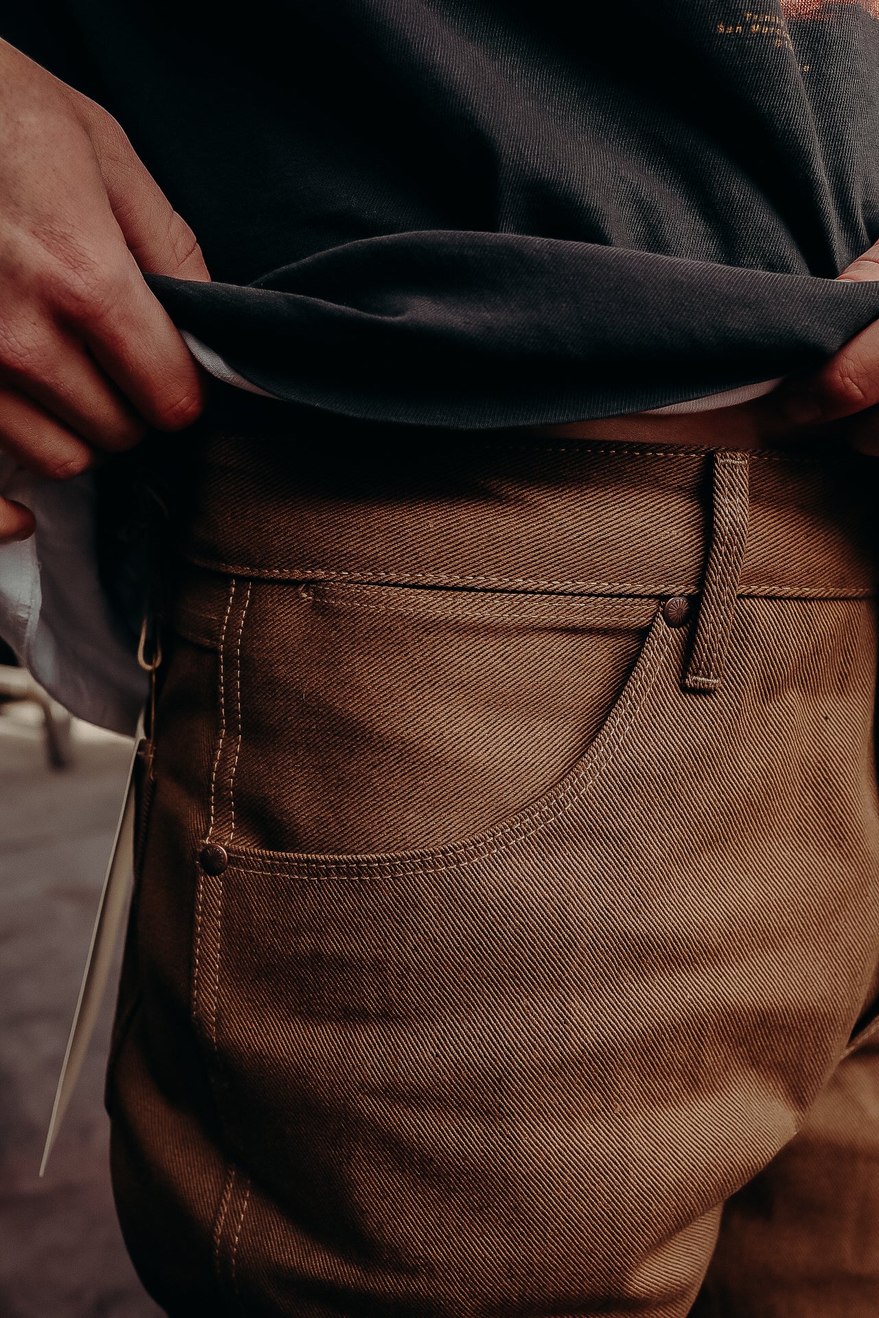 Close-up of person pulling up dark shirt showing brown durable work pants pocket detail