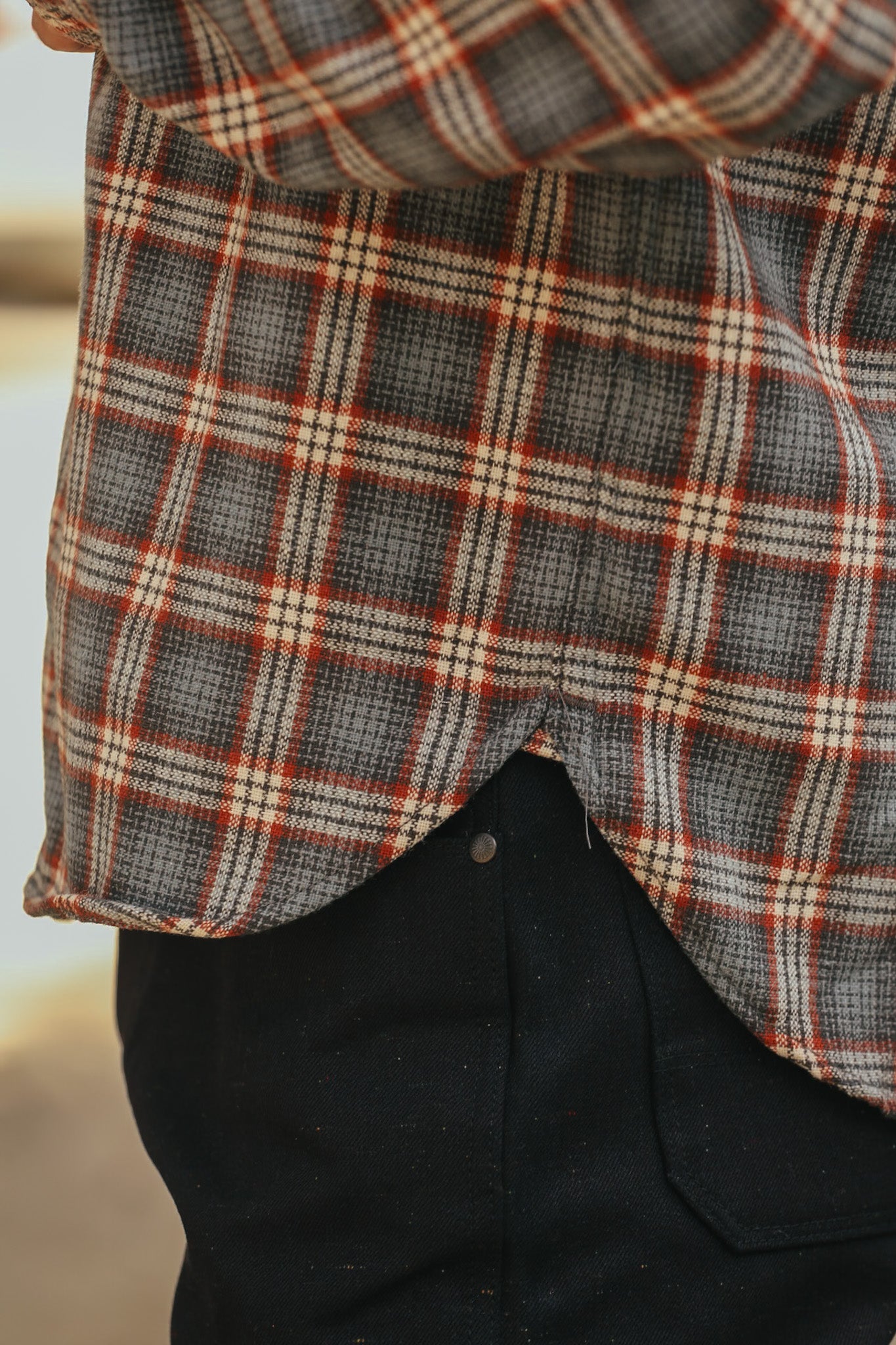 Close-up of person wearing a grey and red plaid shirt over black denim jeans