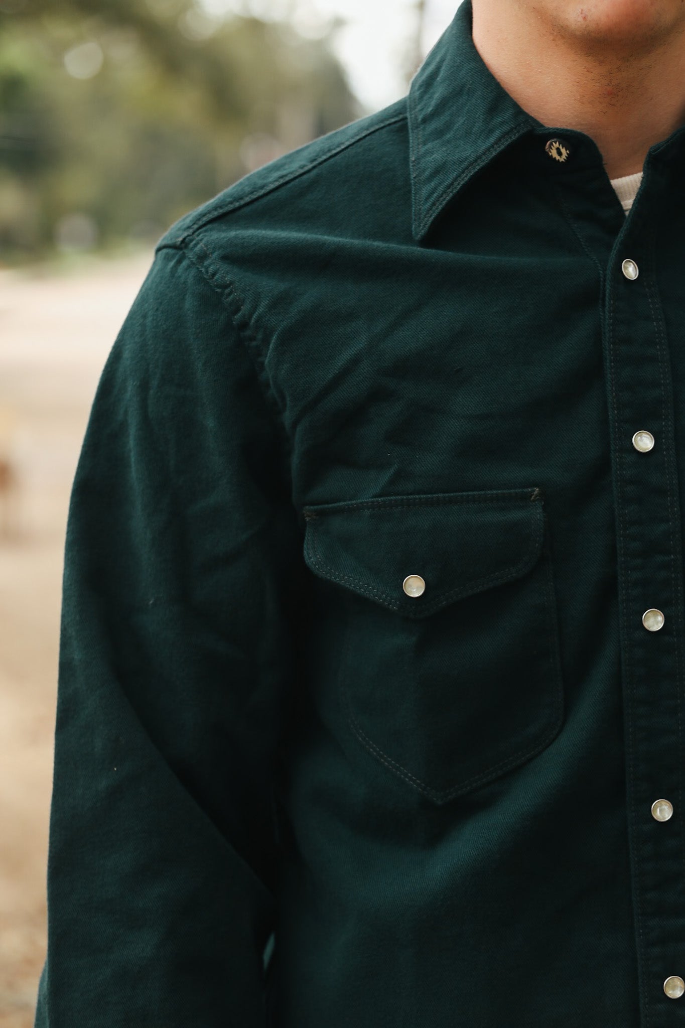 Close-up of a man wearing a dark green rugged work shirt with pearl snap buttons and a flap pocket outdoors