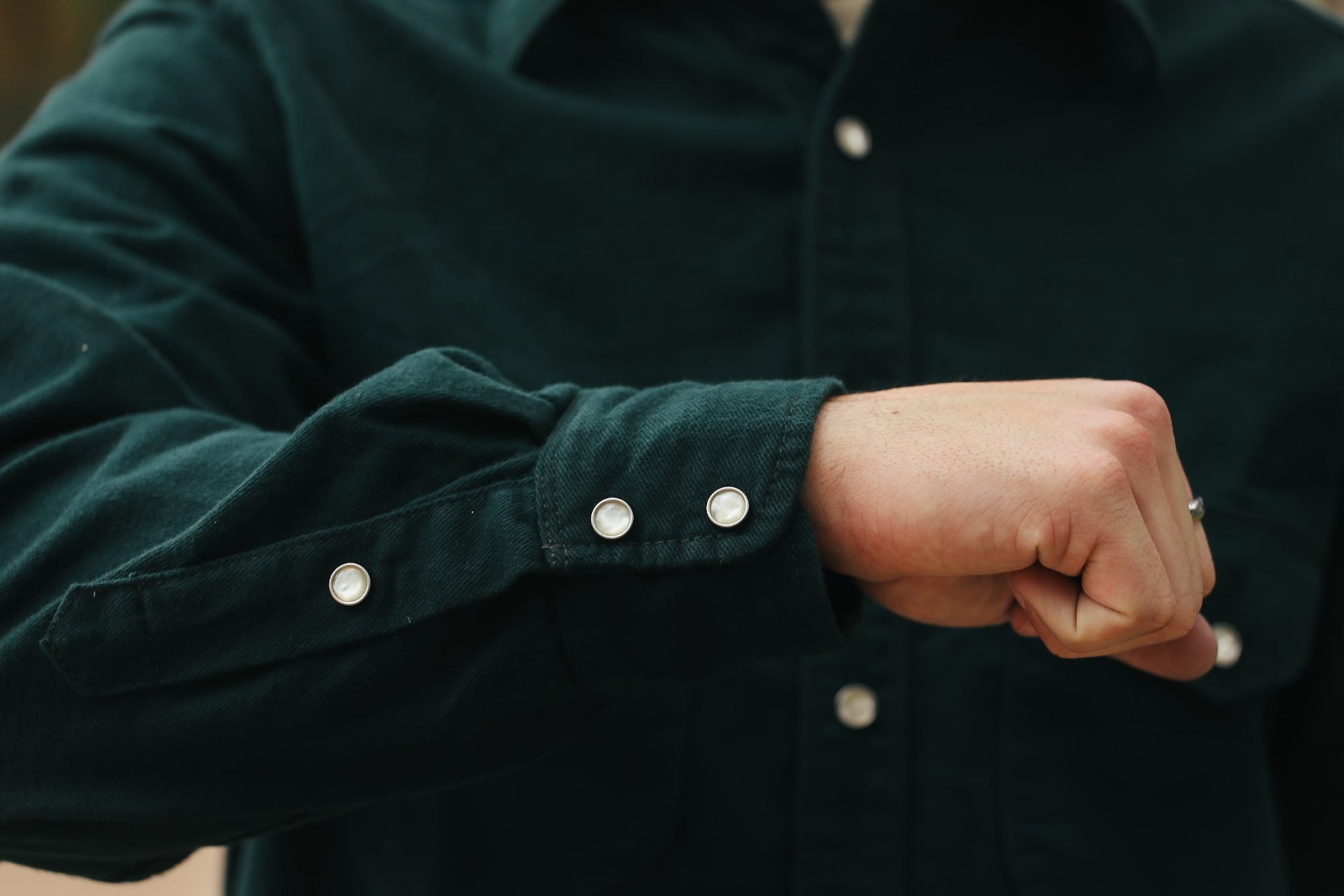 Close-up of a person's arm in a dark green button-up shirt with pearl snap buttons, showing cuff details