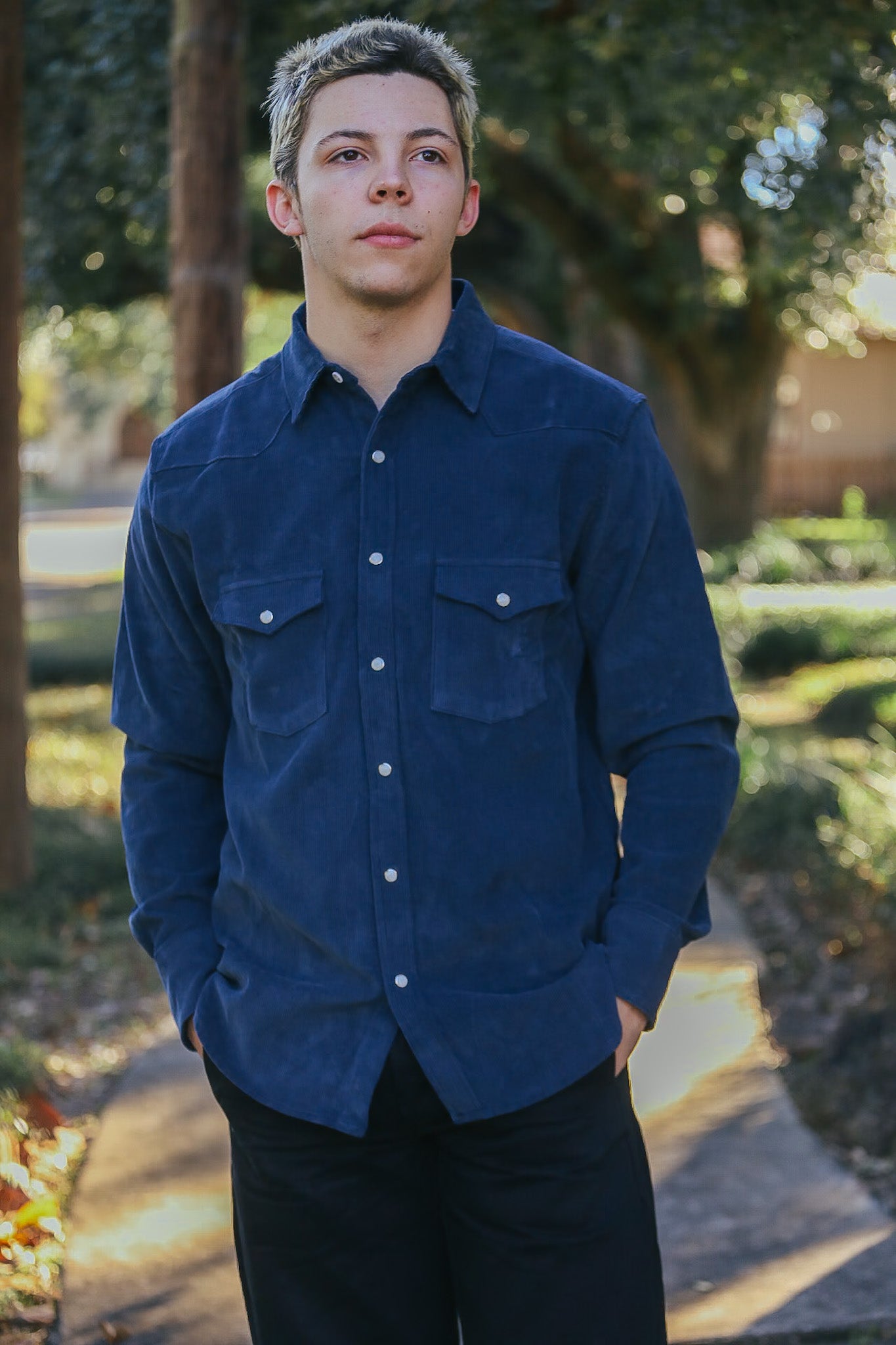 Young man wearing navy blue button-up shirt with front pockets outdoors on sunny path