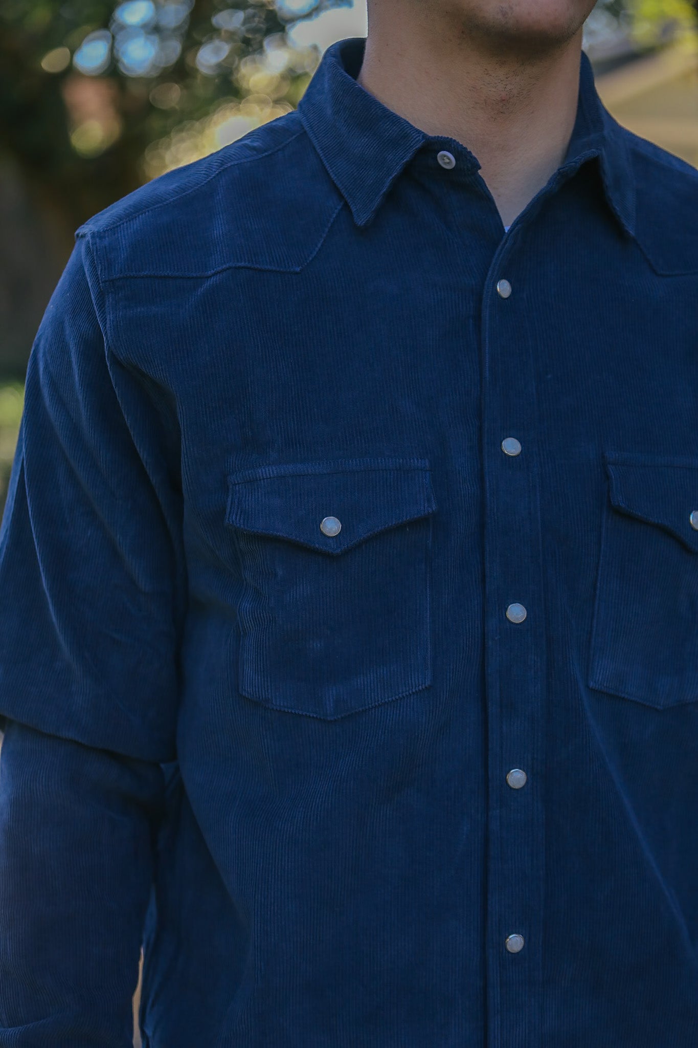 Close-up of a man wearing a dark blue corduroy shirt with buttoned pockets, outdoors