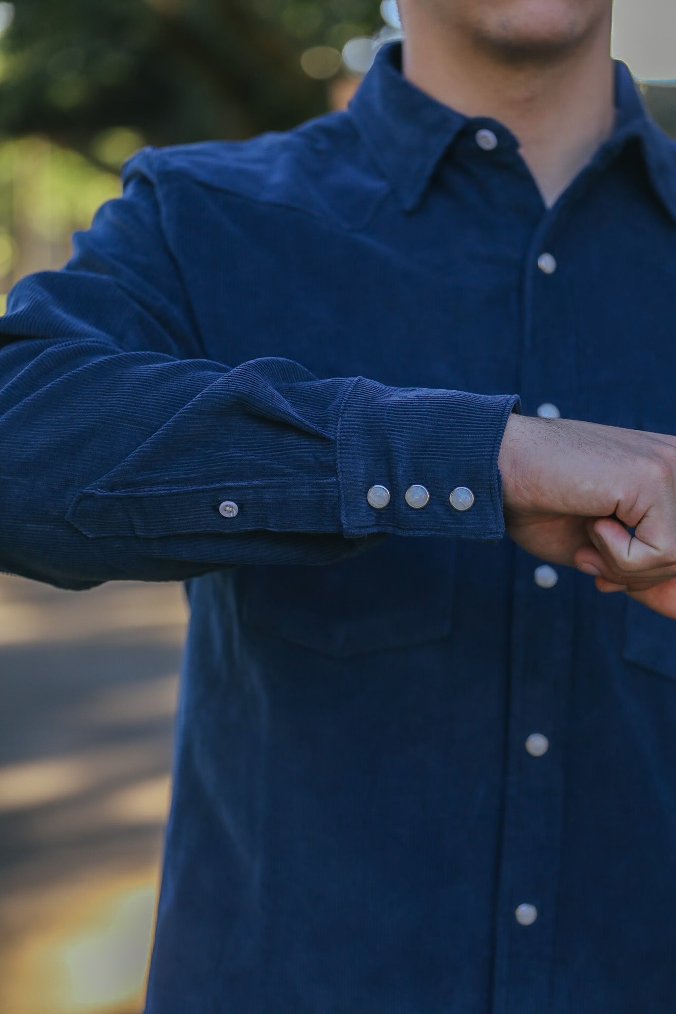 Close-up of a man wearing a blue corduroy shirt with silver snap buttons on cuff and front, outdoors