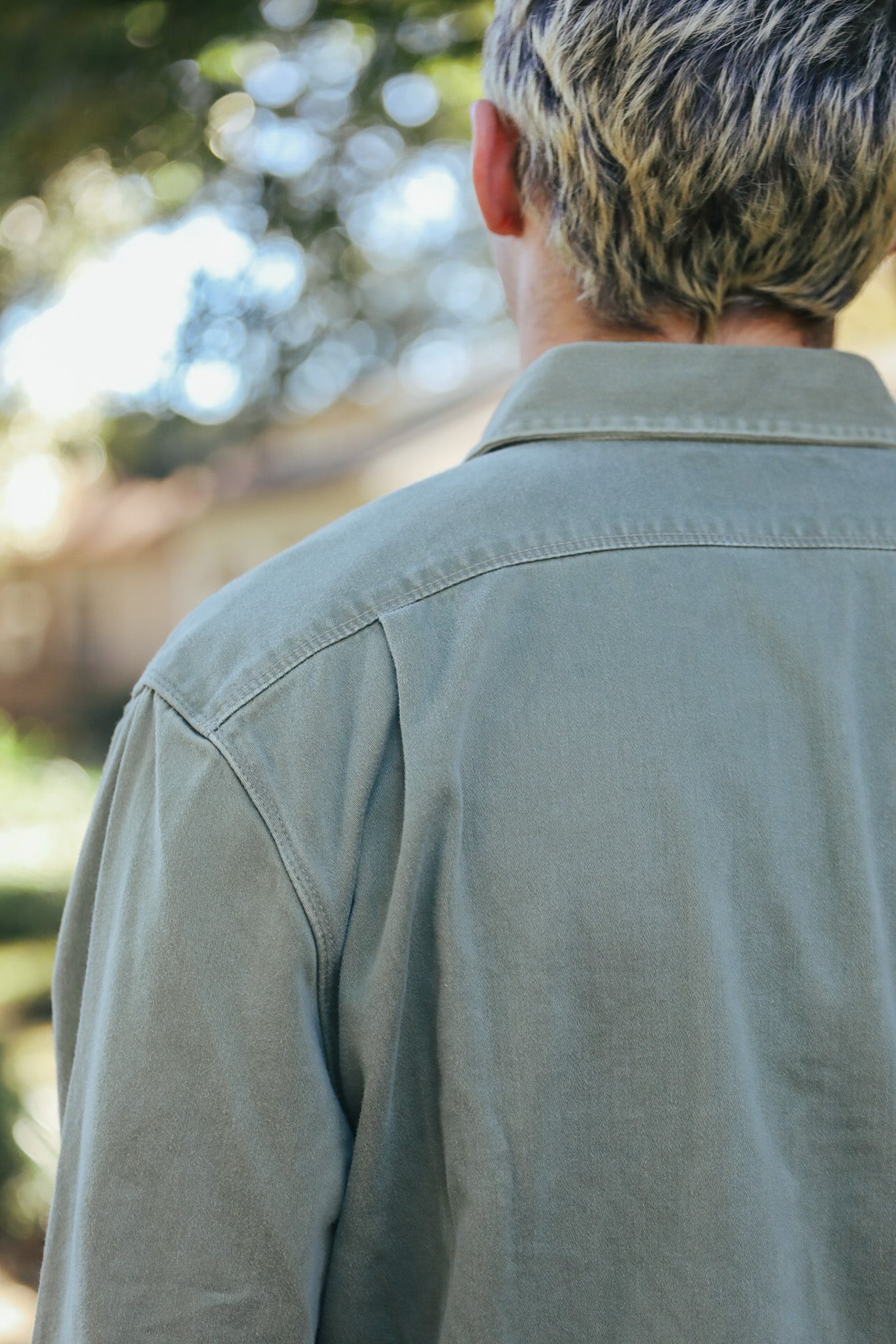 Back view of person with blonde hair wearing green button-up work shirt outdoors