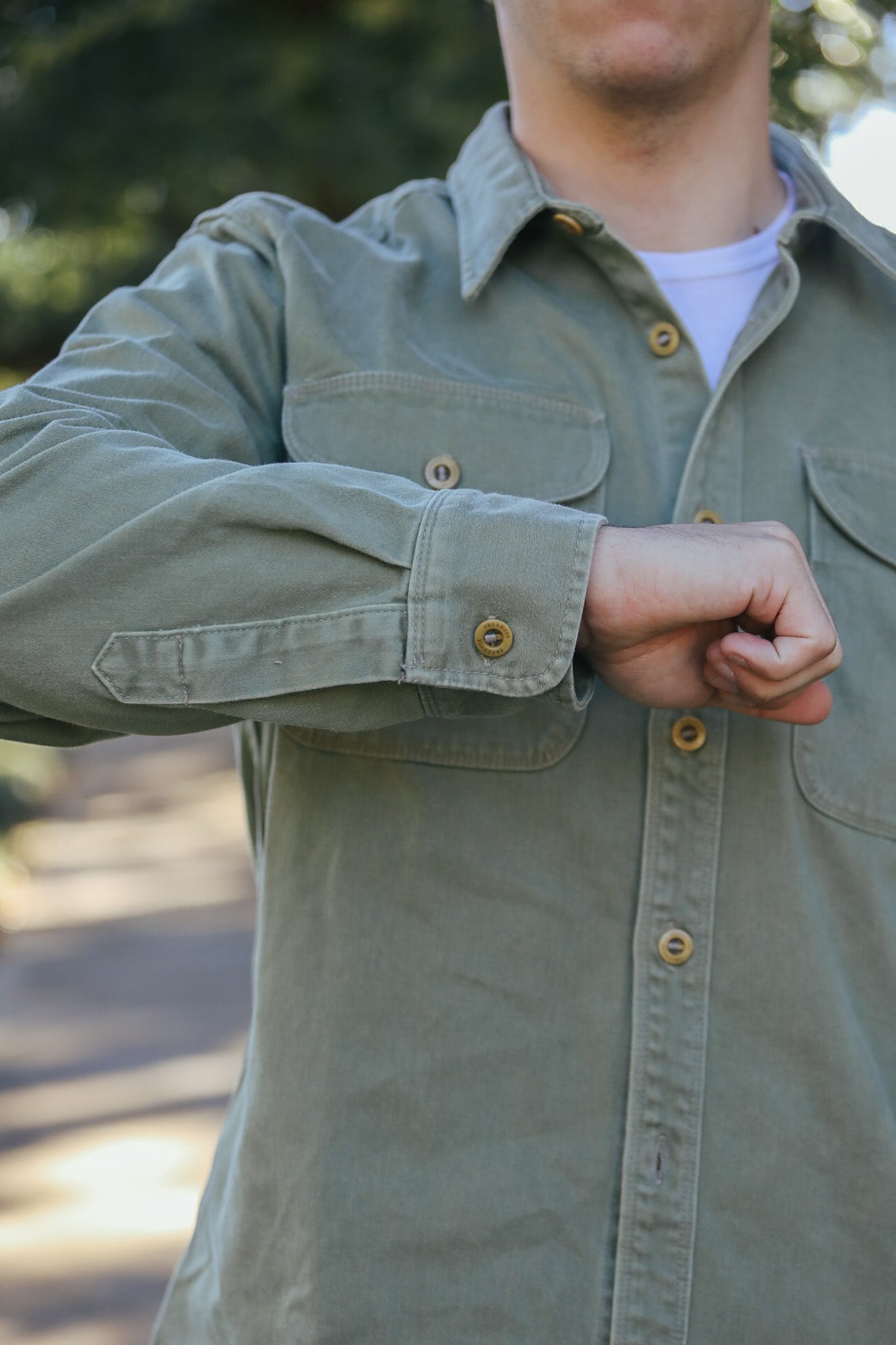 Man wearing olive green button-up shirt with front pockets and rolled sleeves outdoors