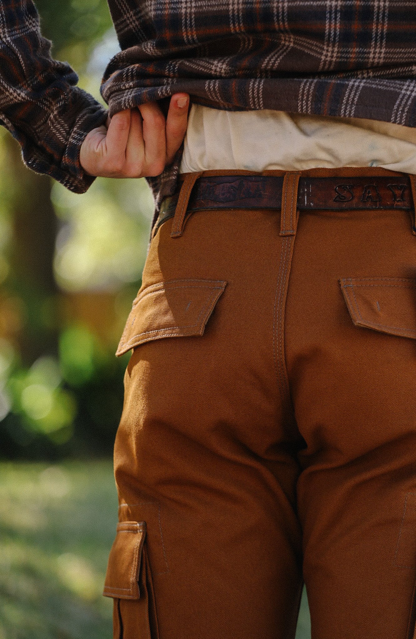 Close-up of person wearing brown work pants with cargo pockets and a leather belt outdoors