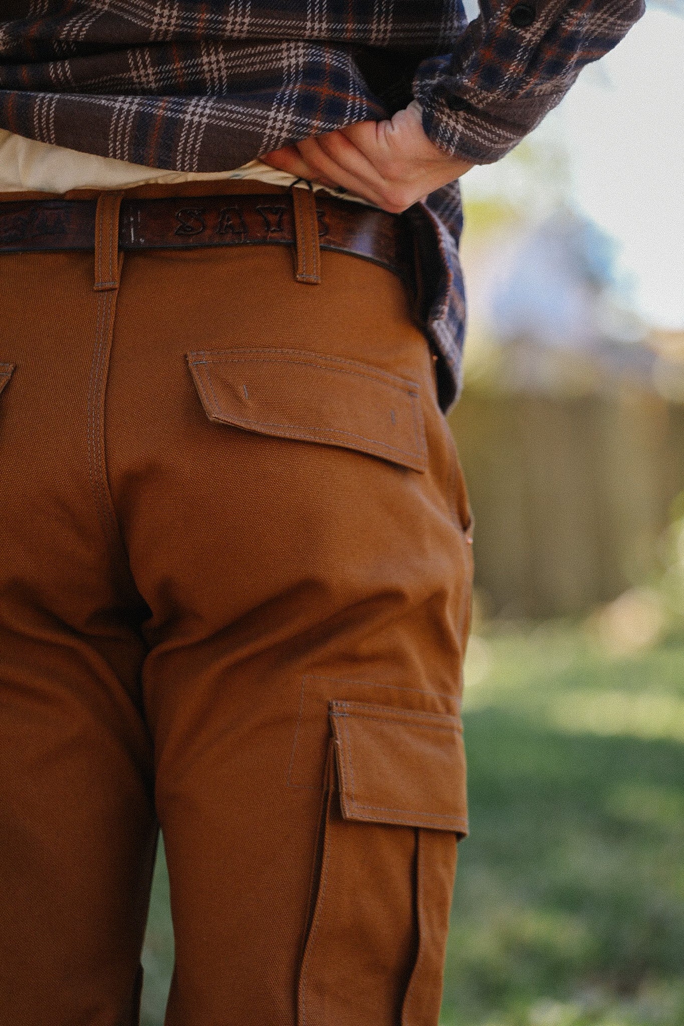 Close-up of person wearing brown cargo work pants and leather belt with plaid shirt outdoors