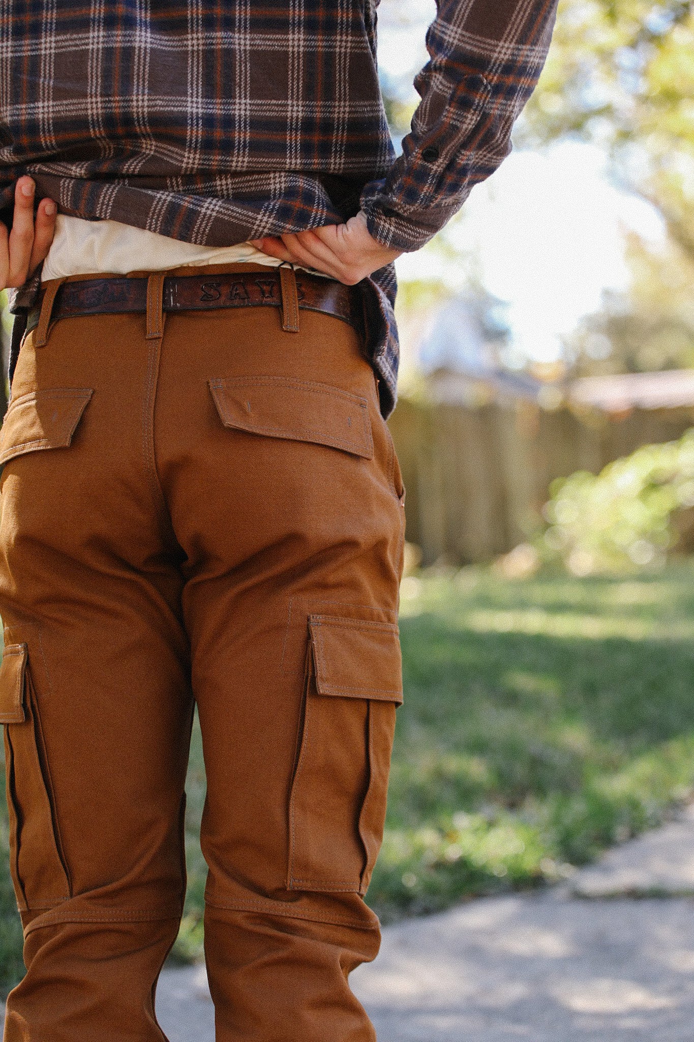 Man wearing brown work pants with cargo pockets and a belt, paired with a plaid shirt outdoors