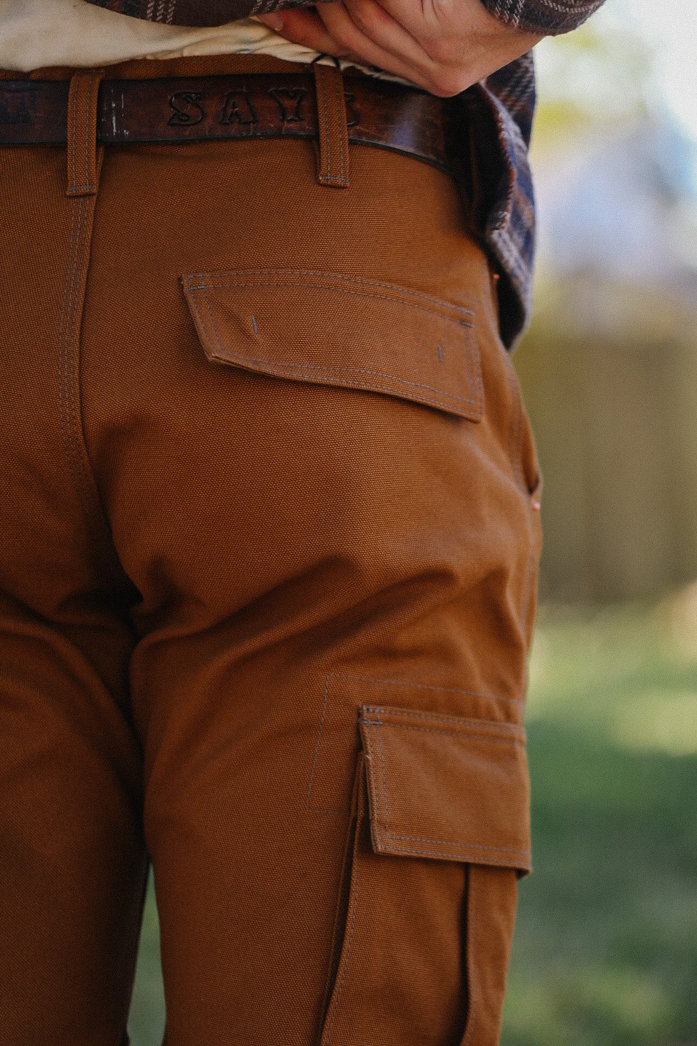 Close-up of rust brown durable work pants with flap pockets and a leather belt outdoors