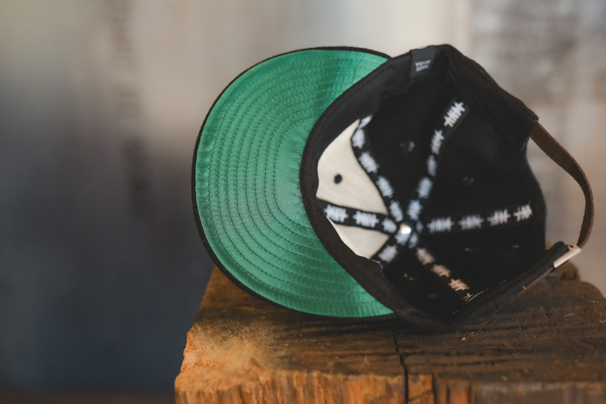 Up close of a black baseball cap on wood block with branding 