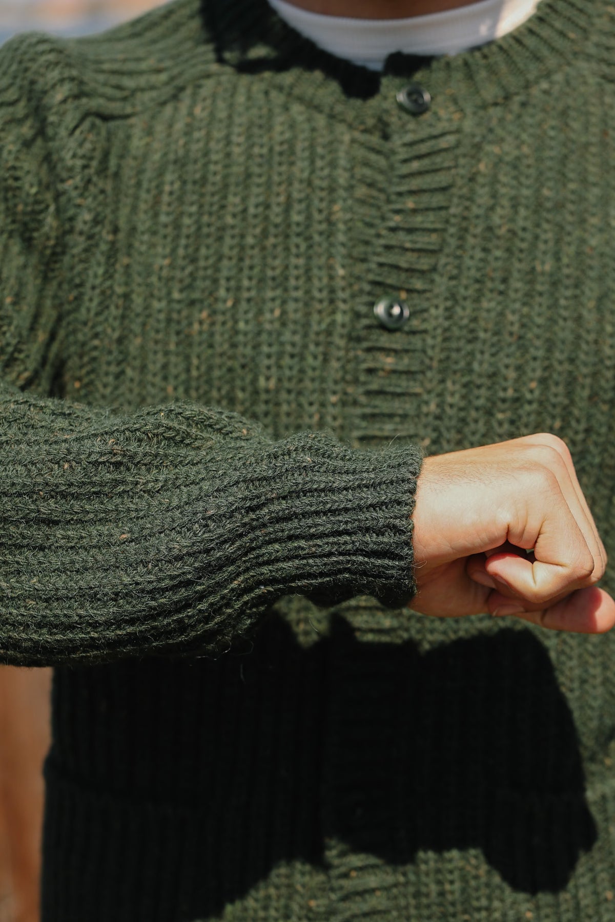 Close-up of a person wearing an olive green ribbed knit cardigan with dark buttons, showing the textured sleeve and hand.