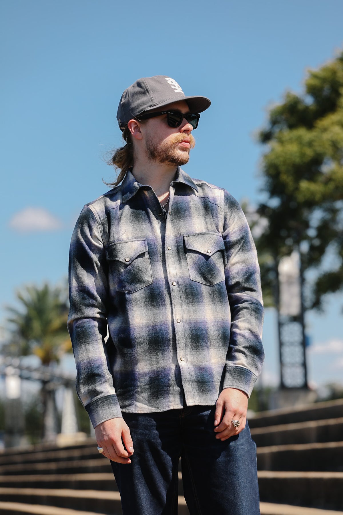 Close-up of a man wearing a blue and gray plaid flannel shirt outdoors, with sunlight casting shadows across the fabric.