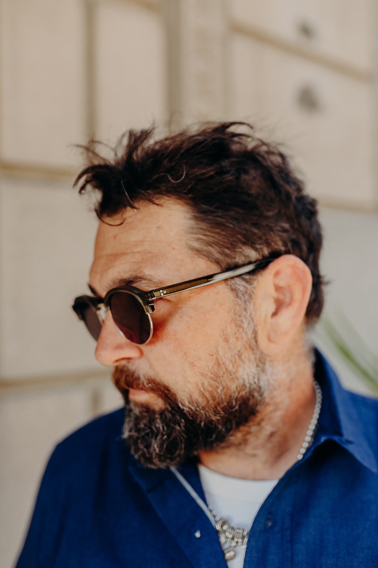 Bearded man wearing round sunglasses and a blue shirt looking sideways outdoors