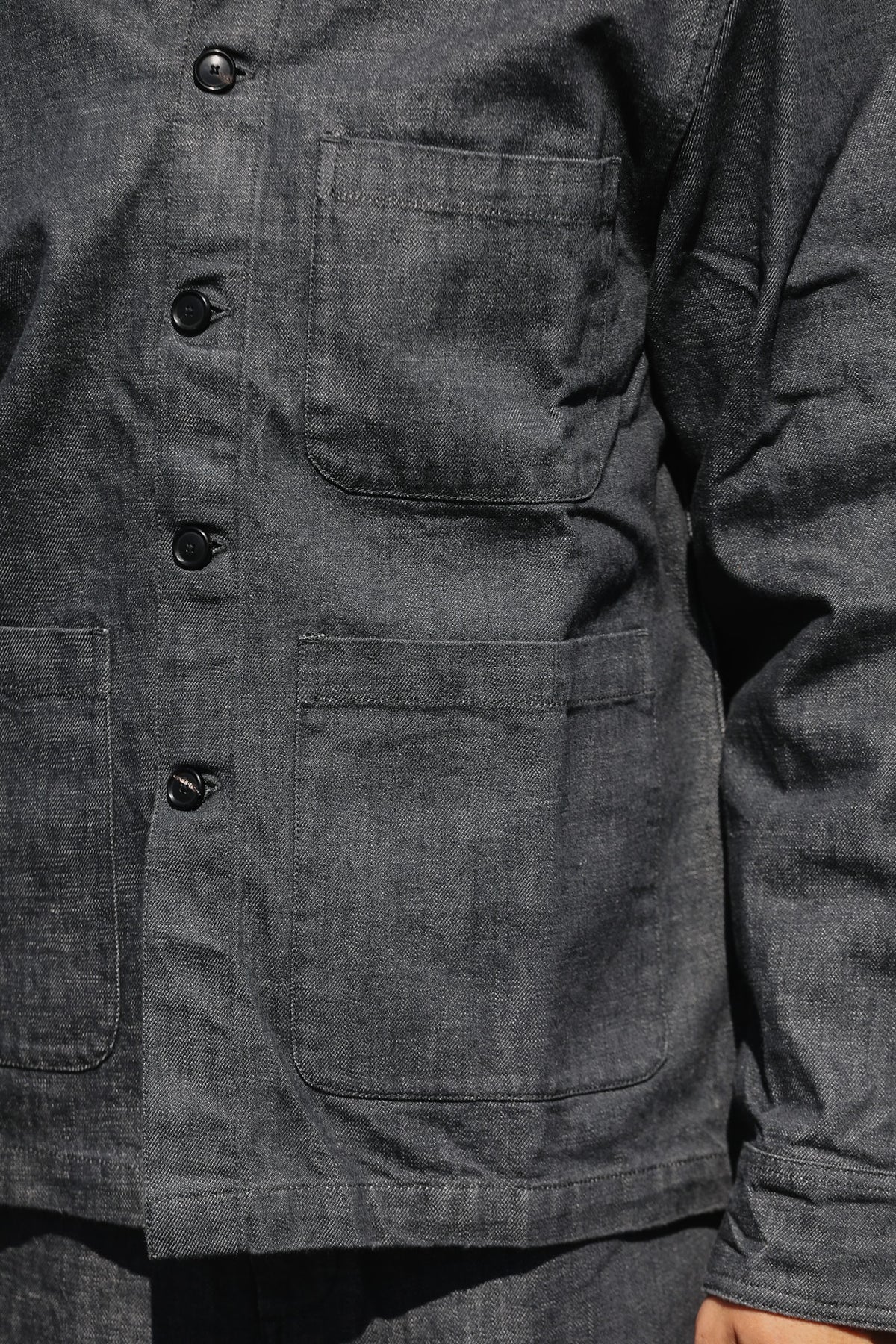 Close-up of a dark charcoal gray denim jacket with a buttoned front and large front pockets.