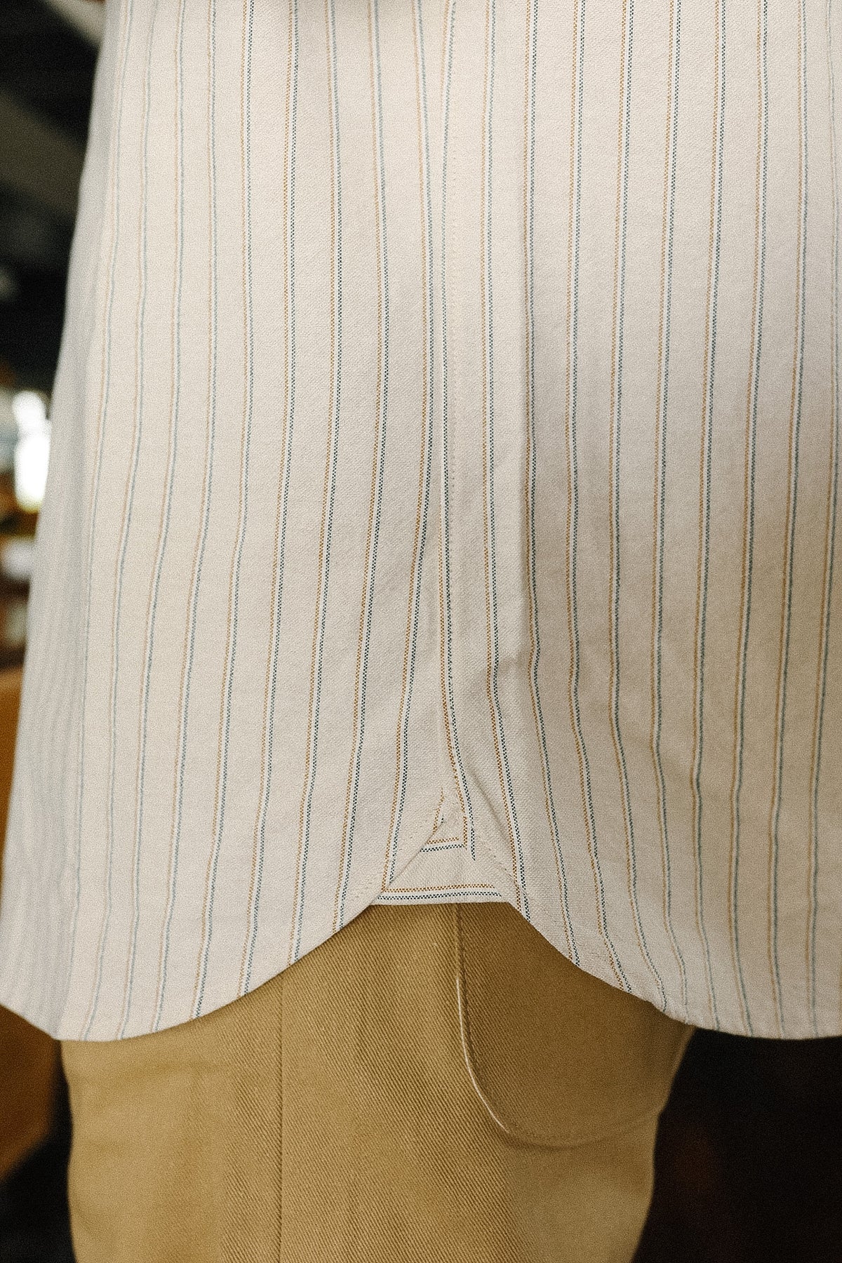 Close-up of a person wearing a beige pinstripe shirt and beige pants.