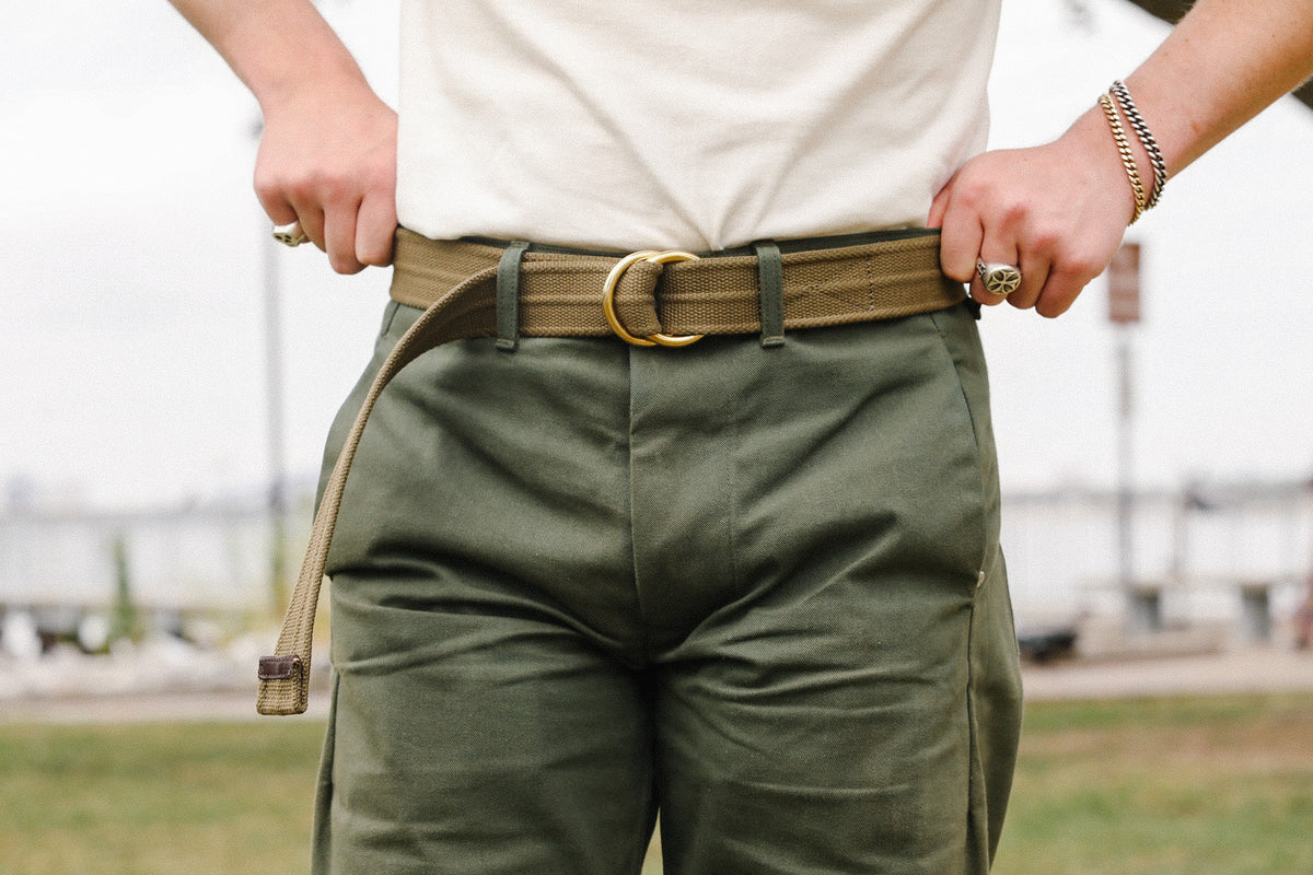 Person wearing olive green pants with a tan canvas belt featuring a double ring buckle outdoors