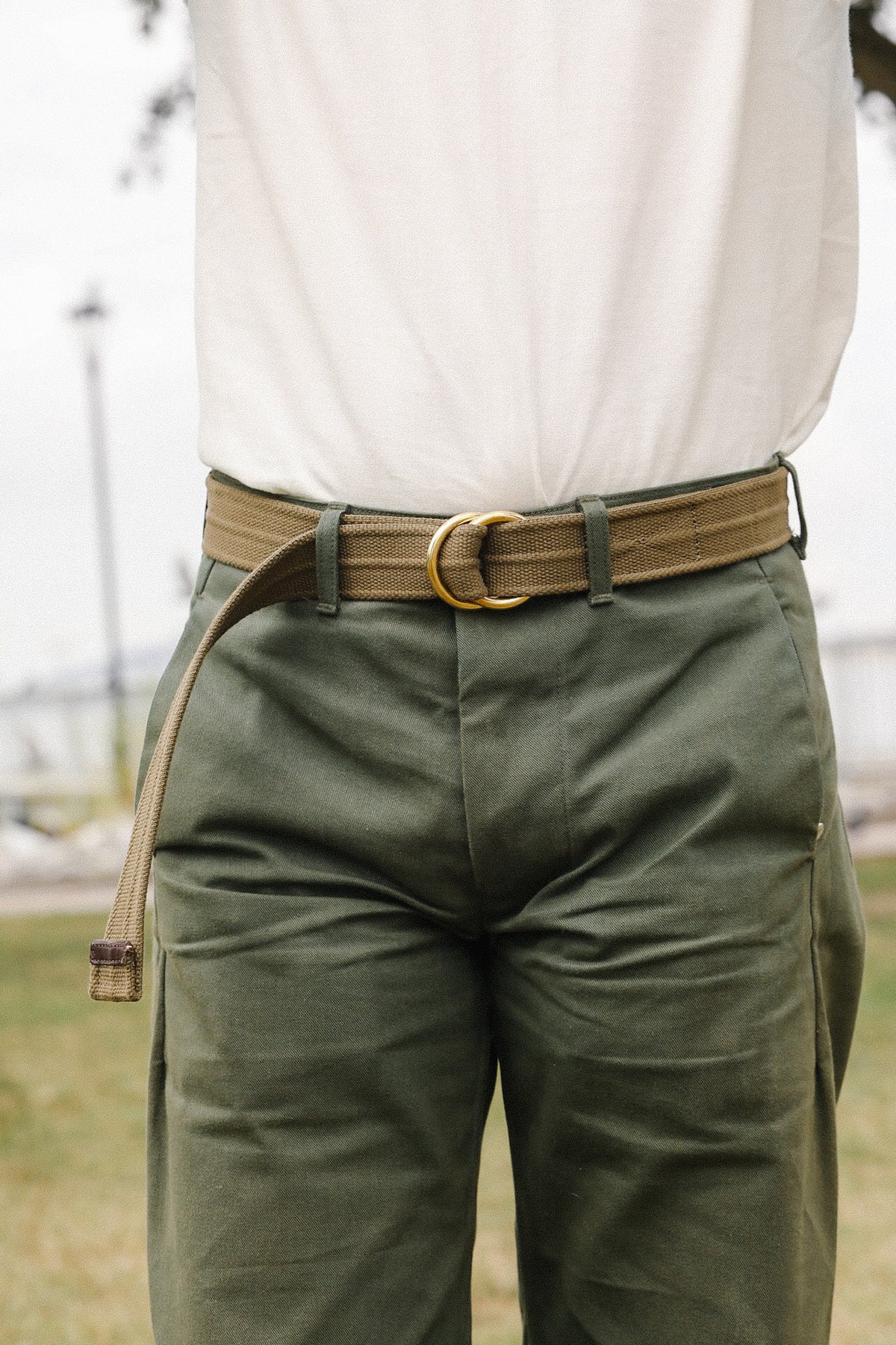 Close-up of person wearing green utility pants with a brown canvas belt and white shirt outdoors