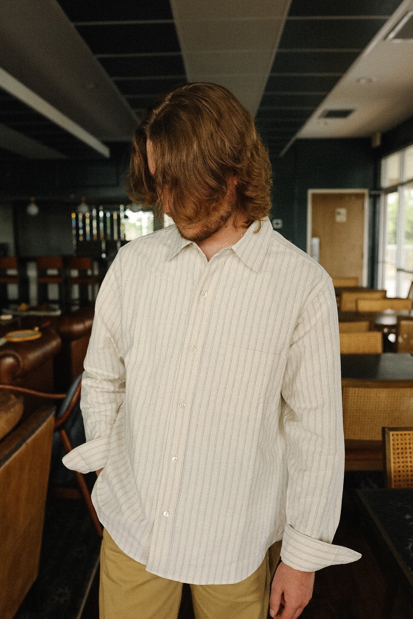 Person wearing a light-colored striped shirt in a room with wooden furniture and a dark ceiling.