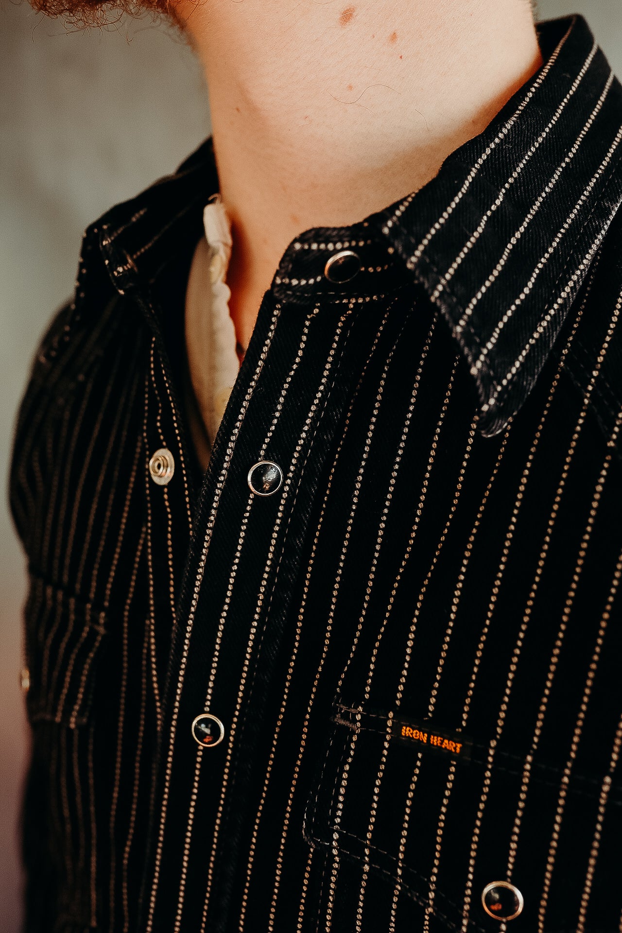 Close-up of a man wearing a black pinstripe Iron Heart shirt with metal snap buttons and collar