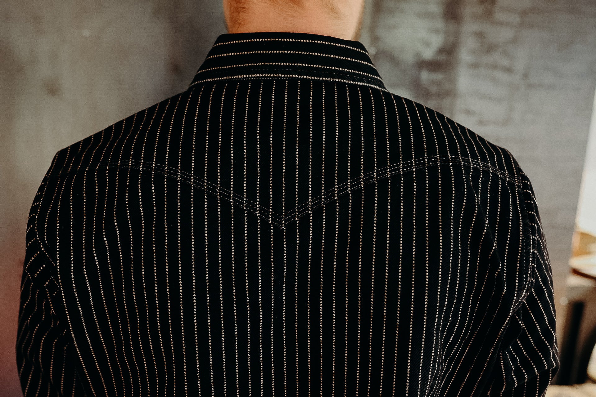 Back view of a person wearing a black long-sleeve shirt with white vertical stripes in an industrial indoor setting