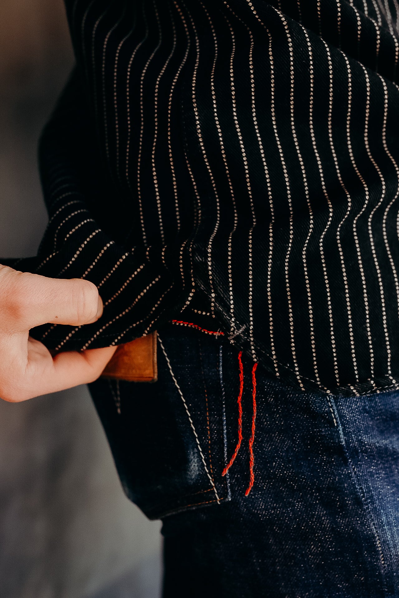 Close-up of a person adjusting black pinstripe shirt tucked into dark denim jeans with red stitching