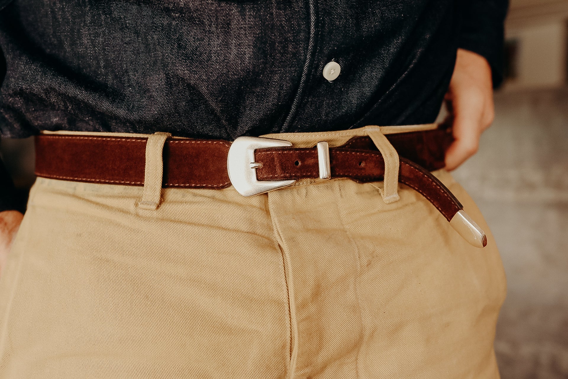 Close-up of brown leather belt with silver buckle worn with beige pants and dark denim shirt