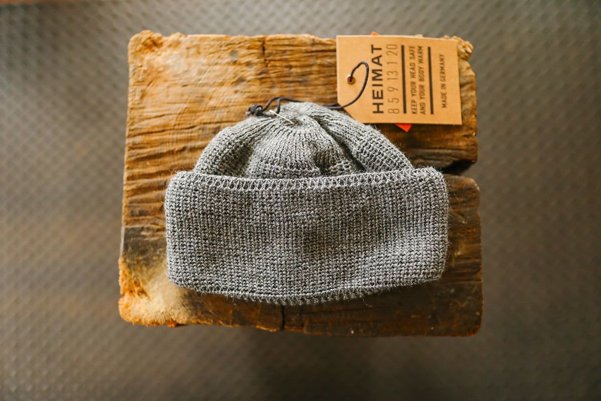 Gray knit beanie with Heimata tag on rustic wooden surface, warm winter headwear