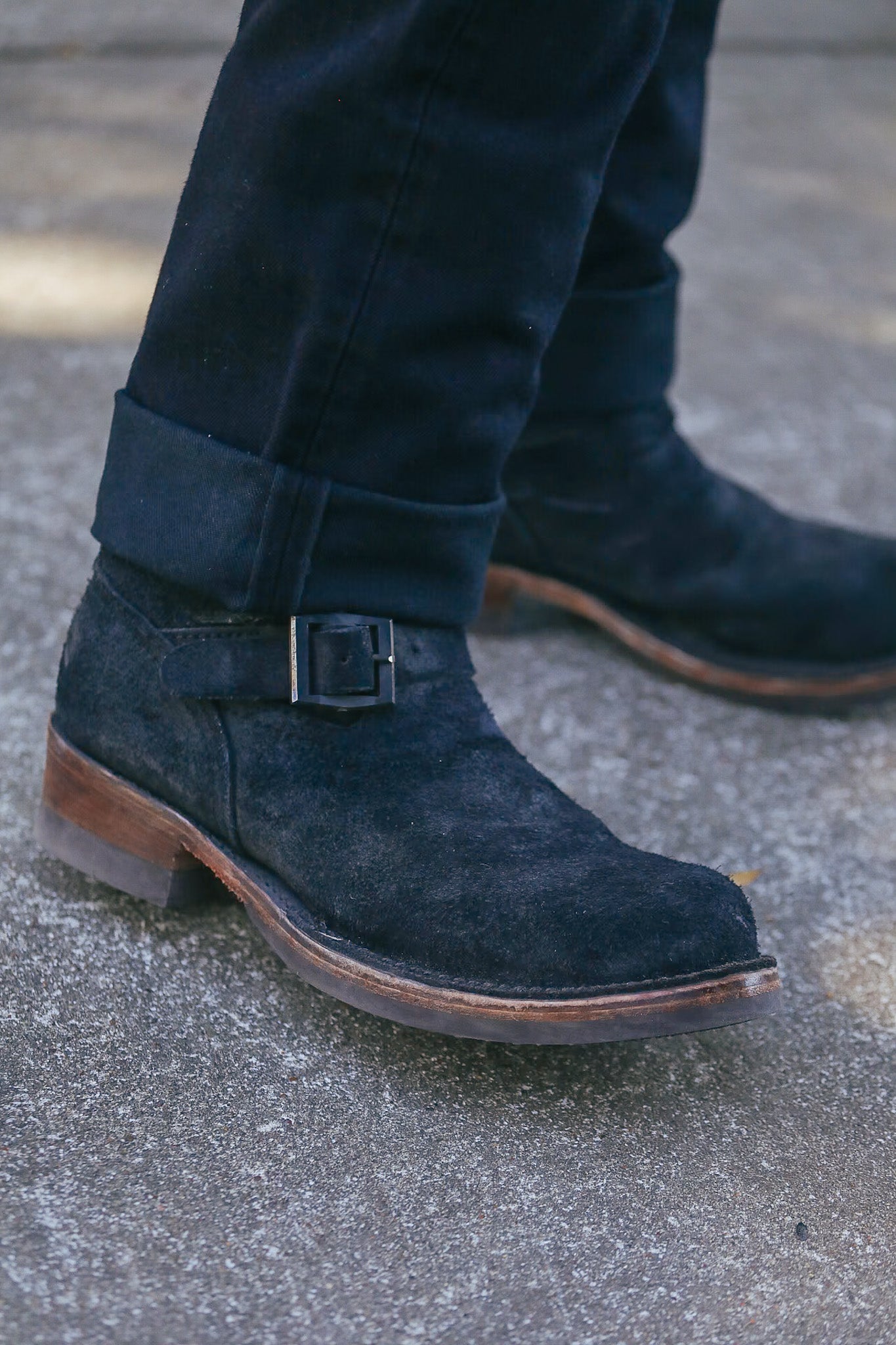 Close-up of black suede leather ankle boots with buckle detail and wooden sole on concrete surface