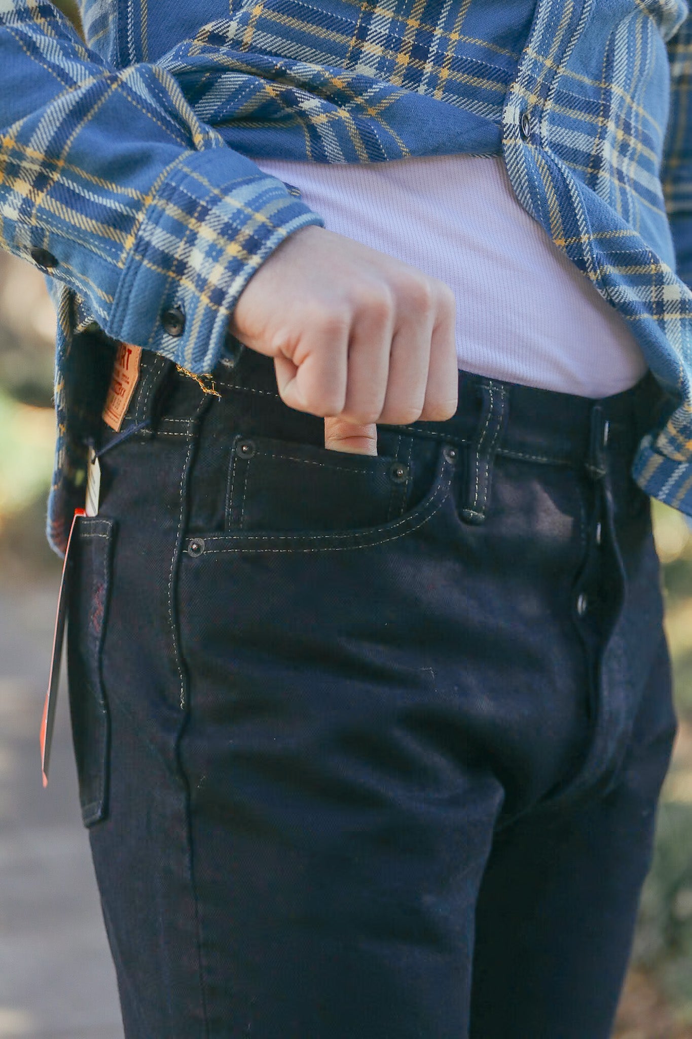 Close-up of person in blue plaid shirt and black denim jeans with hand in front pocket