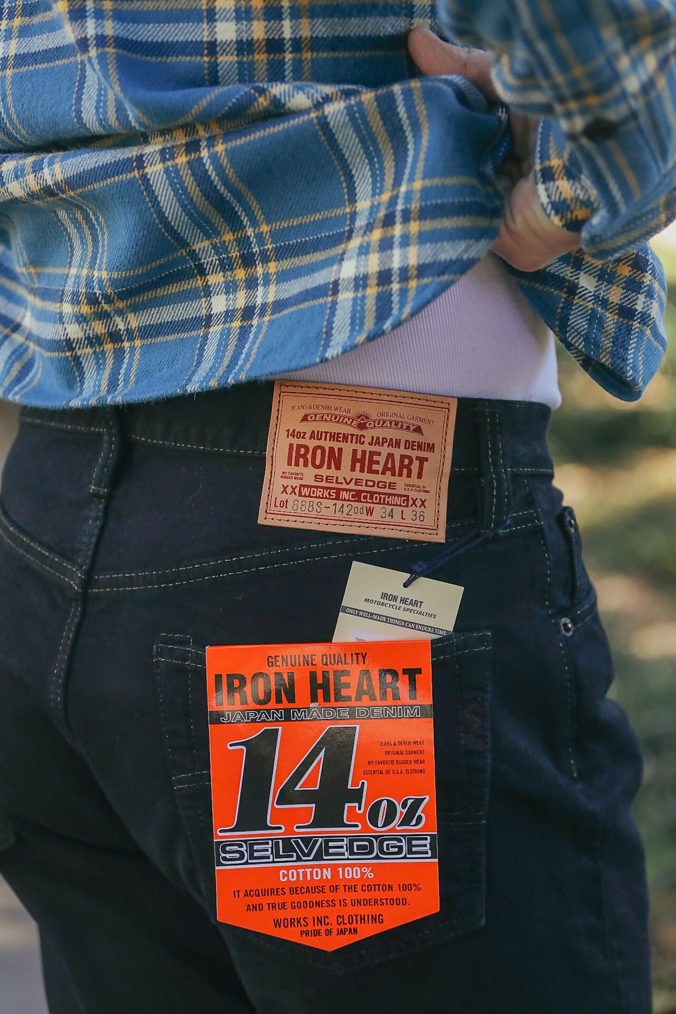 Close-up of person wearing dark Iron Heart 14oz selvedge denim jeans with branded leather patch and orange label
