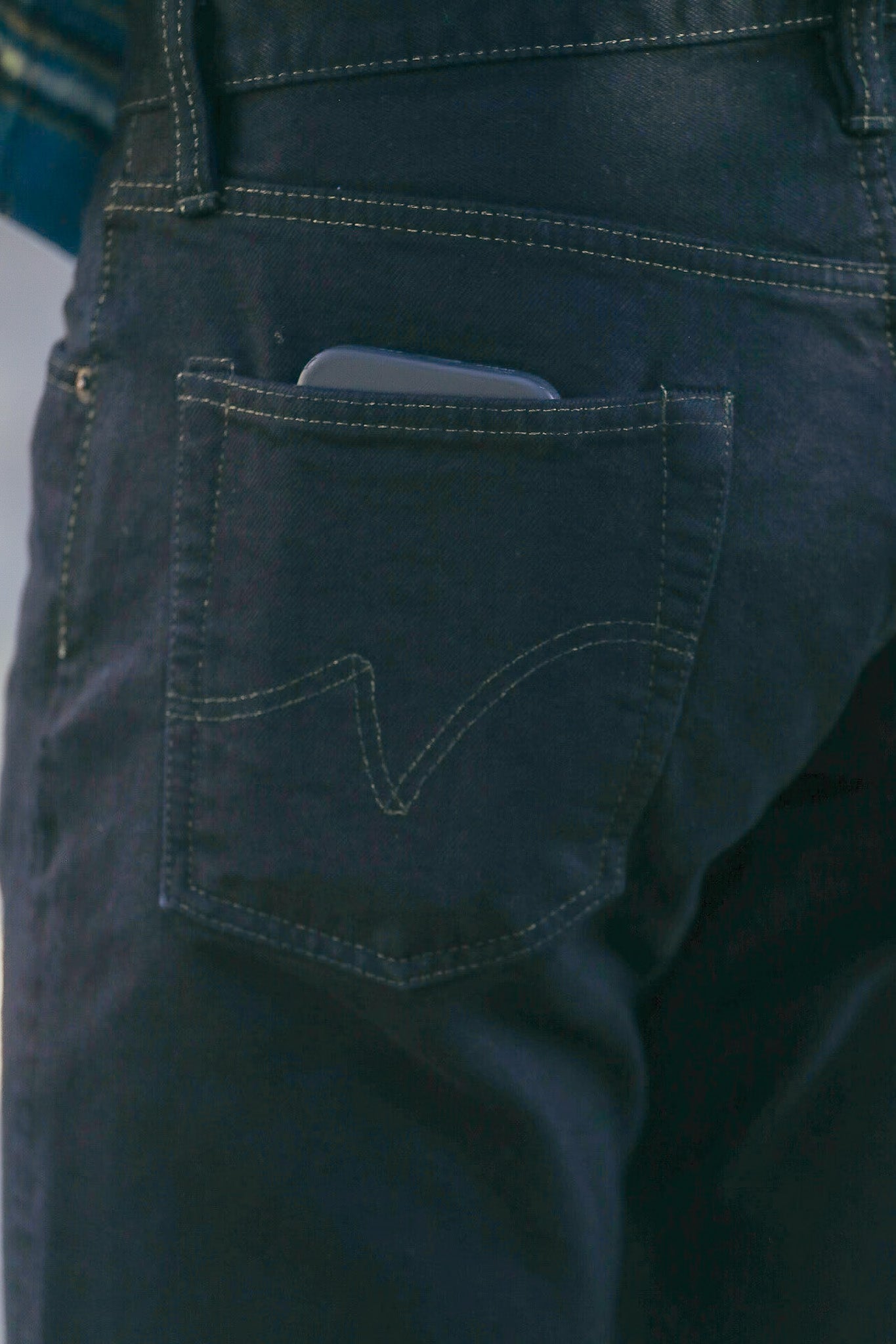 Close-up of a person wearing dark denim jeans with a smartphone partially visible in the back pocket
