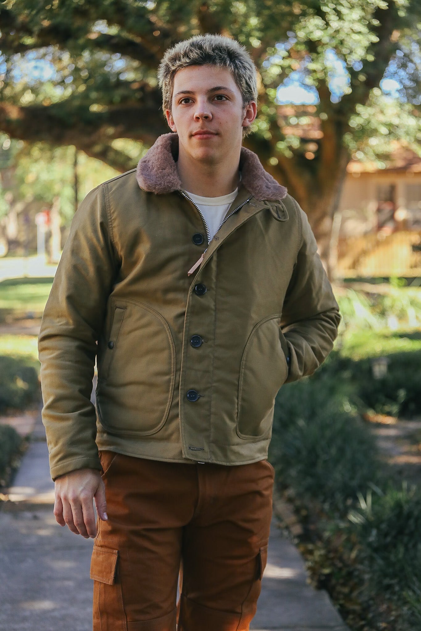 Young man wearing a brown canvas jacket with shearling collar and brown cargo pants outdoors