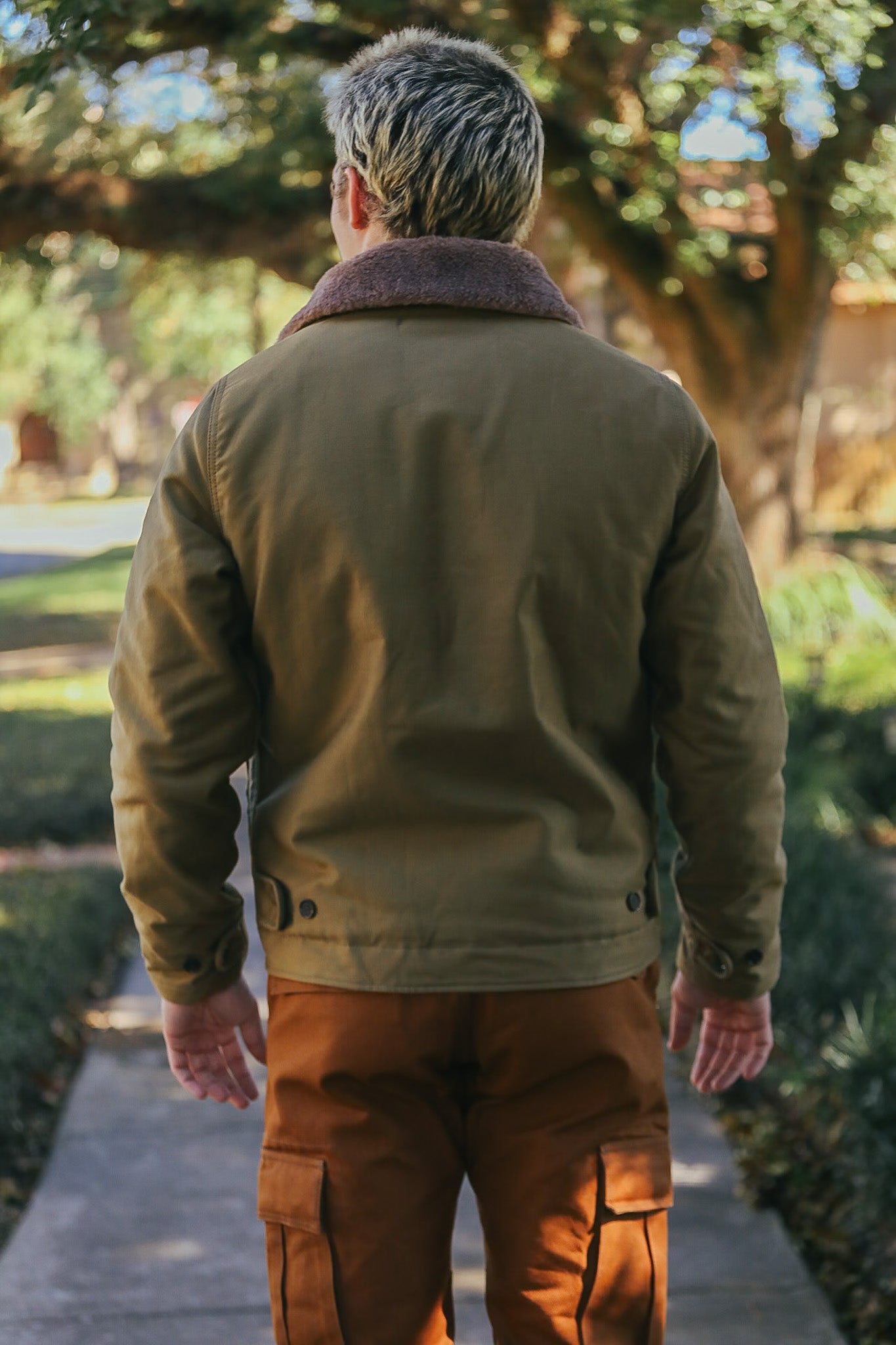 Man wearing olive green jacket with shearling collar and brown cargo pants walking on sidewalk outdoors