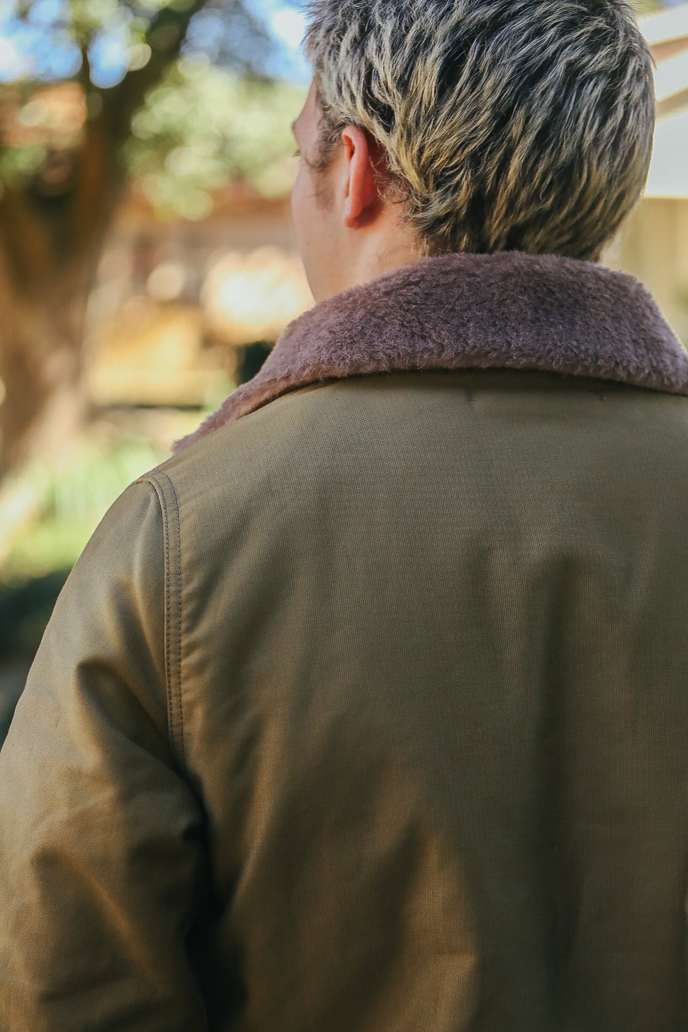 Man wearing olive green jacket with brown fur collar in outdoor setting