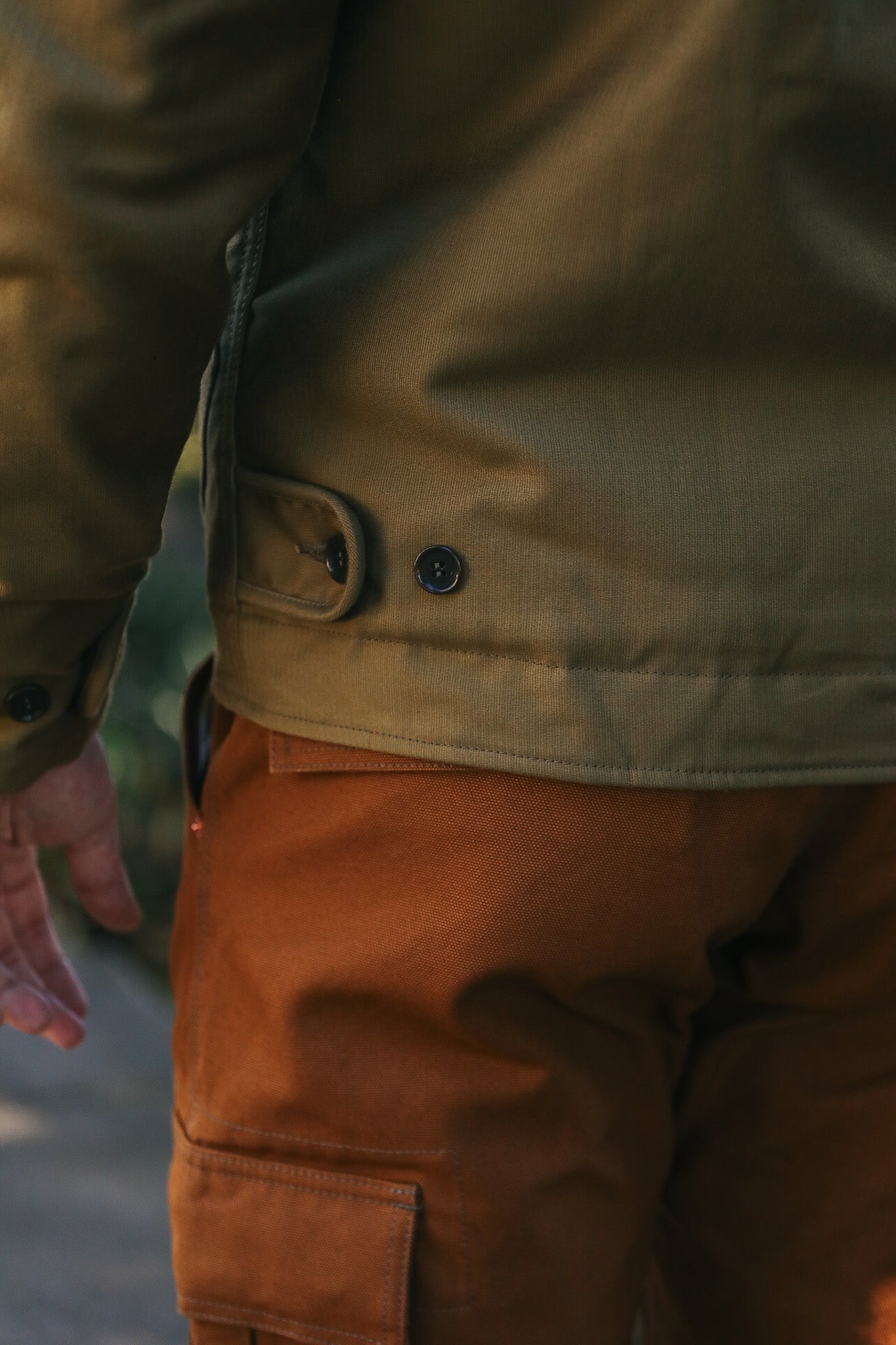 Close-up of person wearing brown canvas work pants and olive green jacket with button details