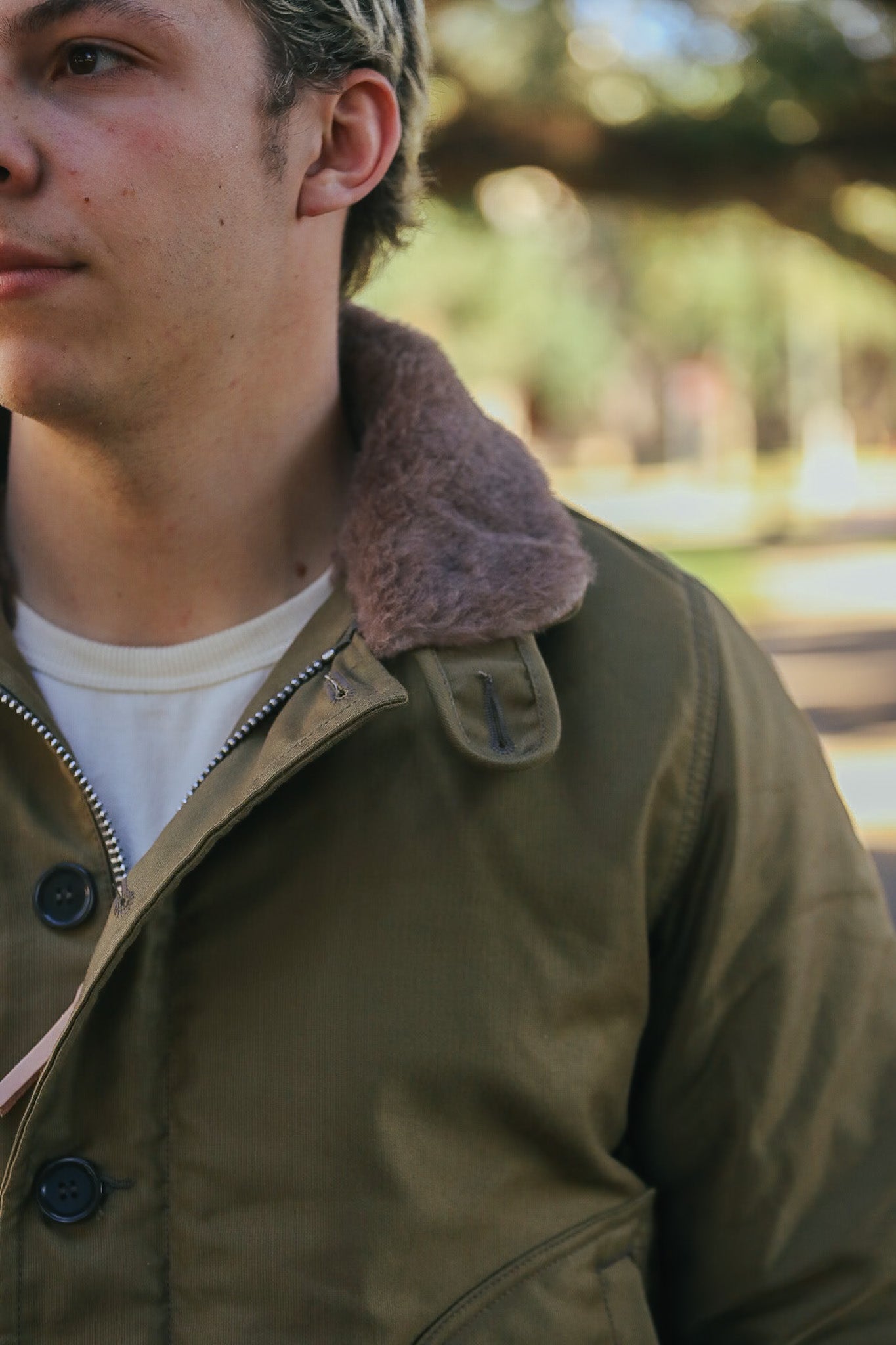 Close-up of man wearing olive green jacket with brown fur collar outdoors in soft sunlight