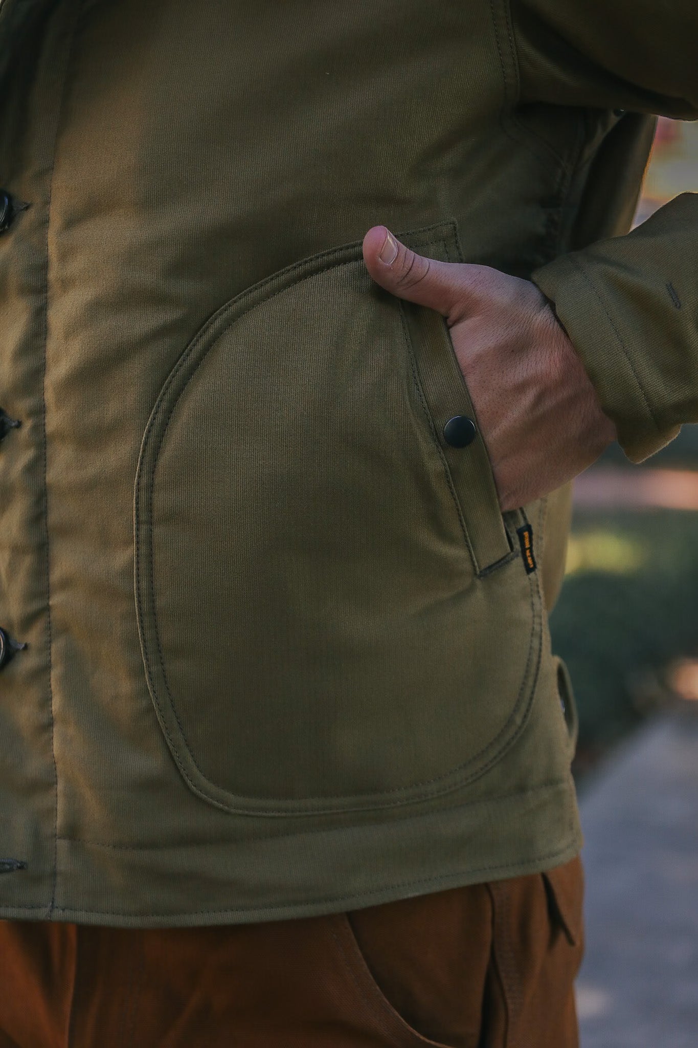 close-up of hand in pocket of olive green rugged work jacket with black snap button at Iron Shop Provisions