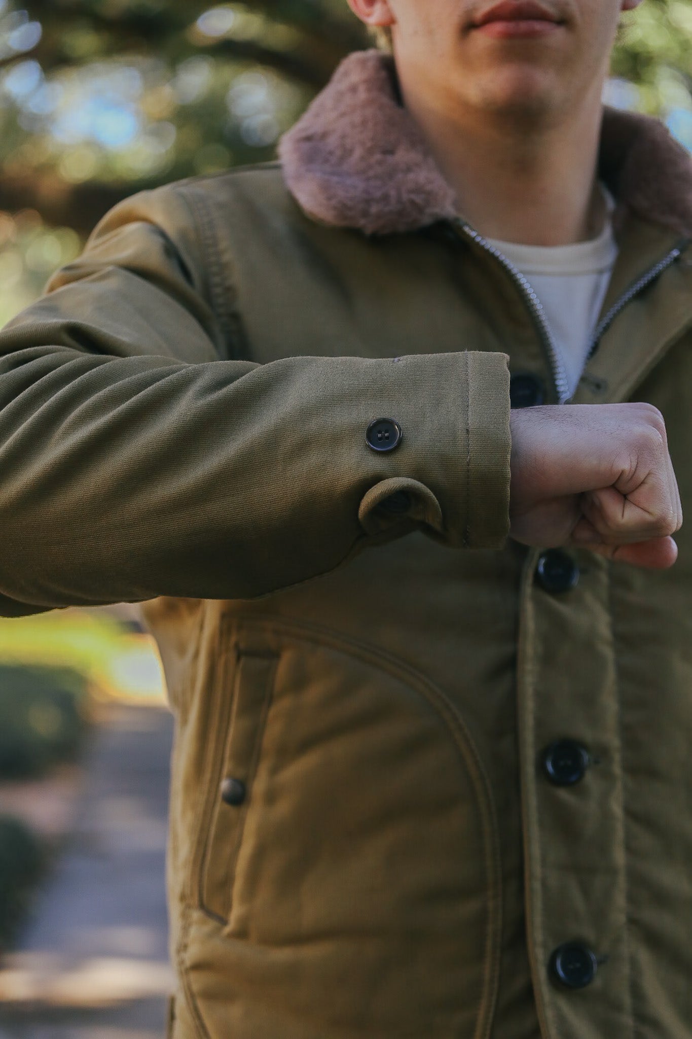 Close-up of a person wearing an olive green button-up jacket with brown shearling collar outdoors