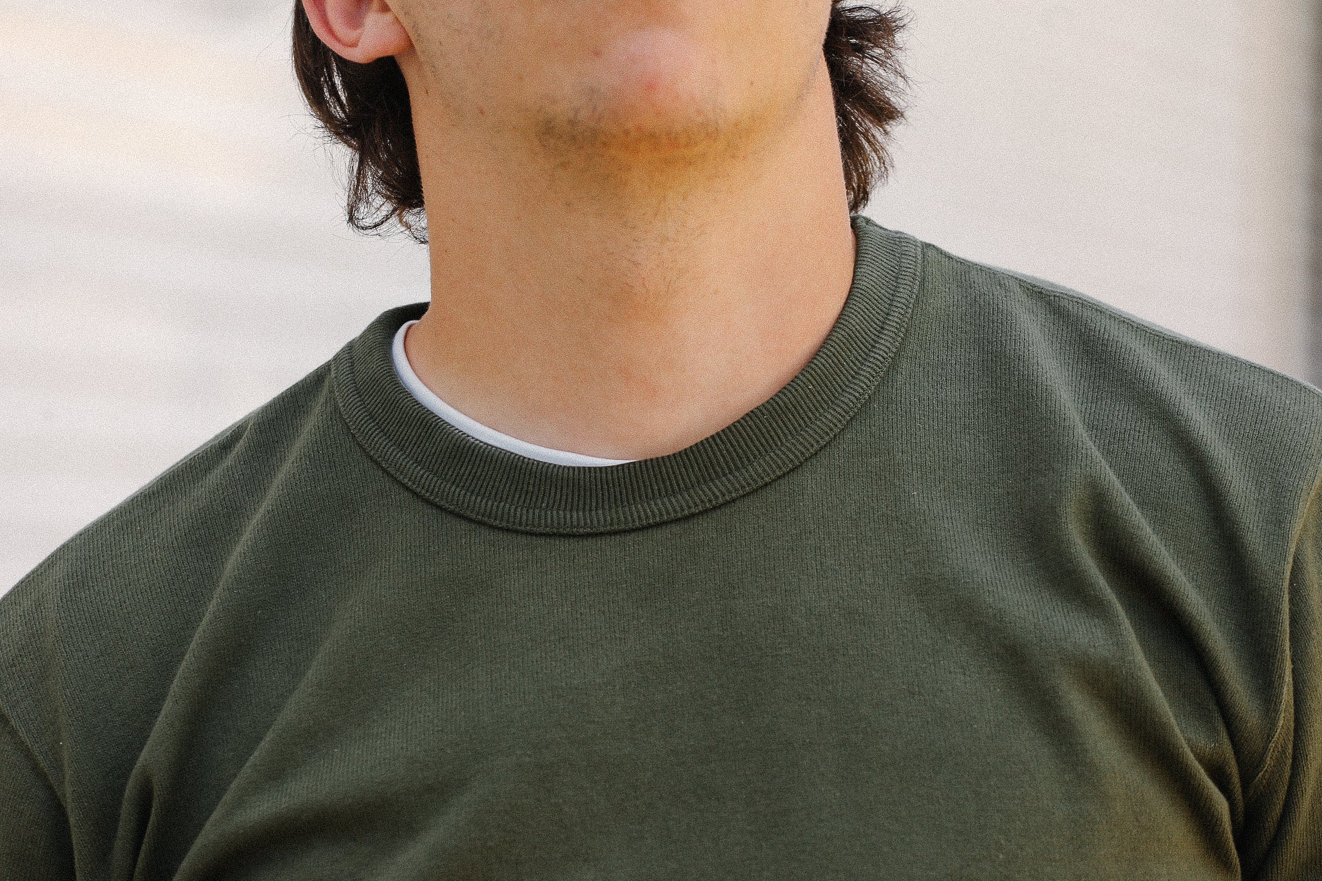 Close-up of a person wearing an olive green crewneck shirt over a white undershirt at Iron Shop Provisions