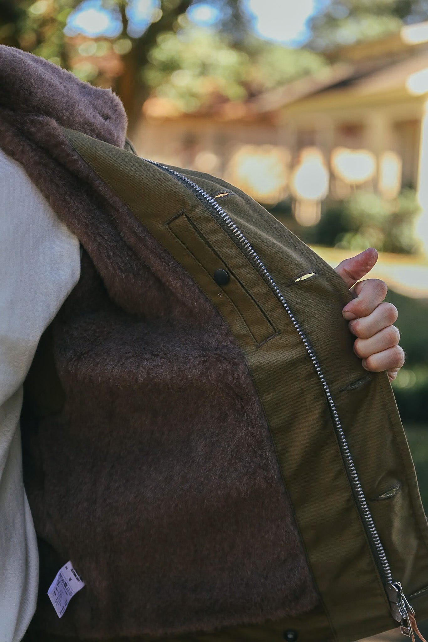 Close-up of hand holding open olive green jacket with brown fleece lining outdoors