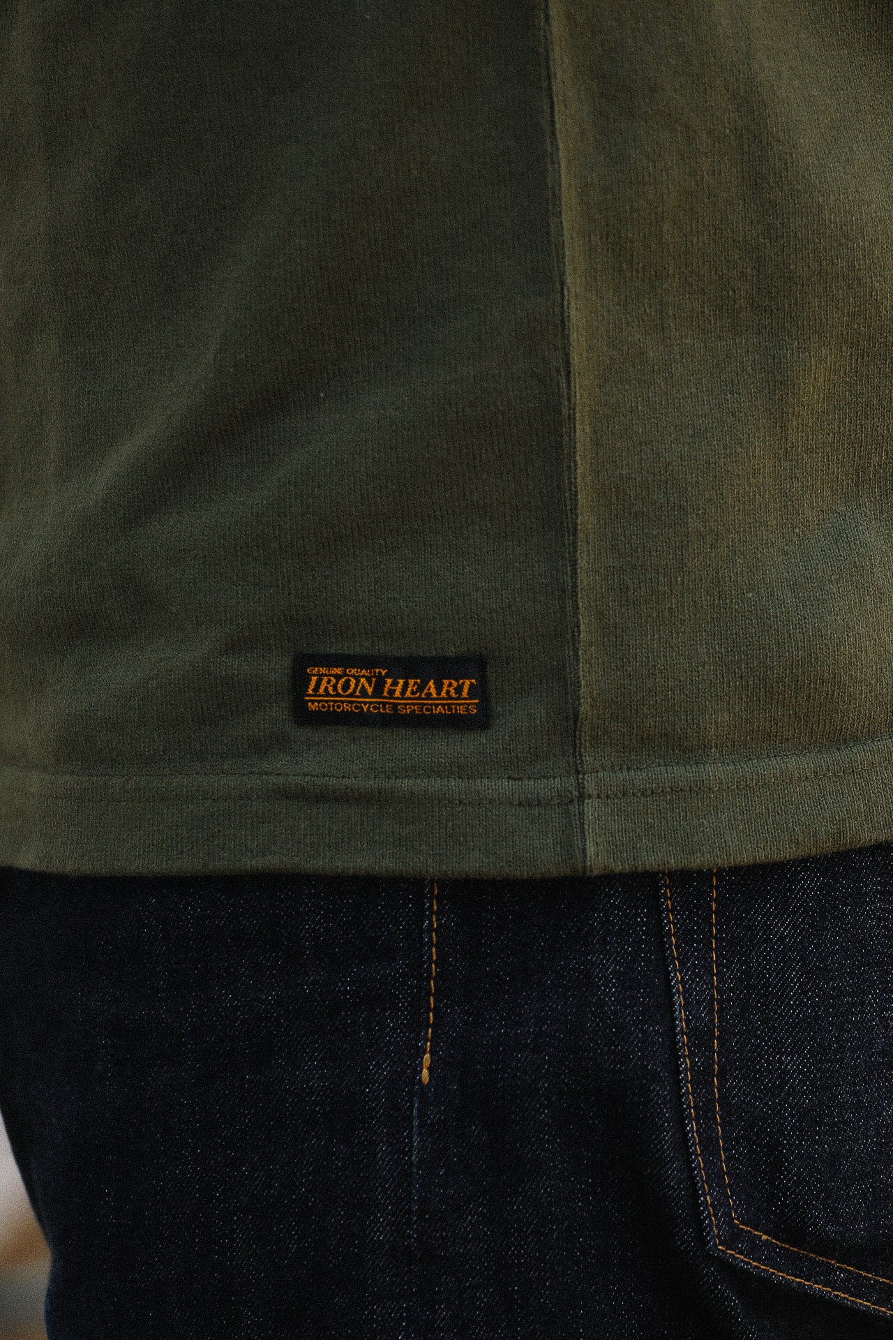 Close-up of dark green Iron Heart T-shirt with brand label above dark blue denim jeans