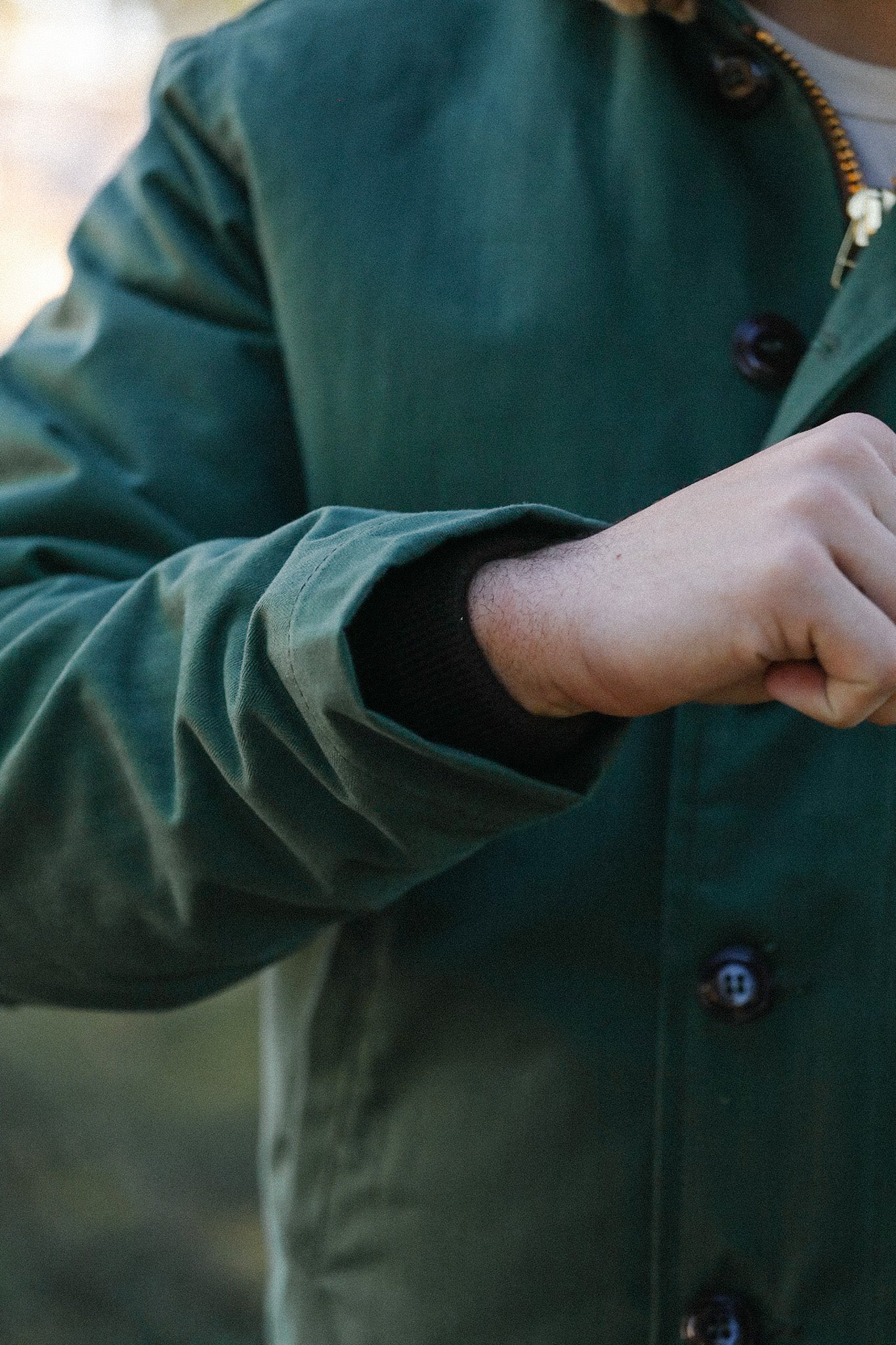 Close-up of a person wearing a green buttoned jacket with black ribbed cuffs, outdoors setting