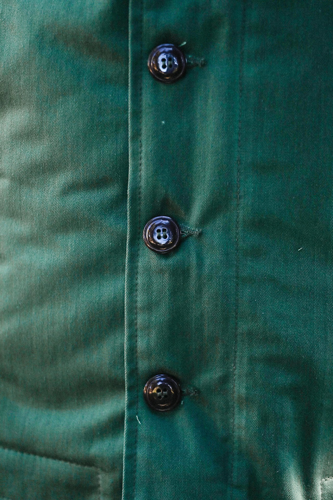 Close-up of dark green buttoned fabric with detailed stitching and texture, Iron Shop Provisions apparel