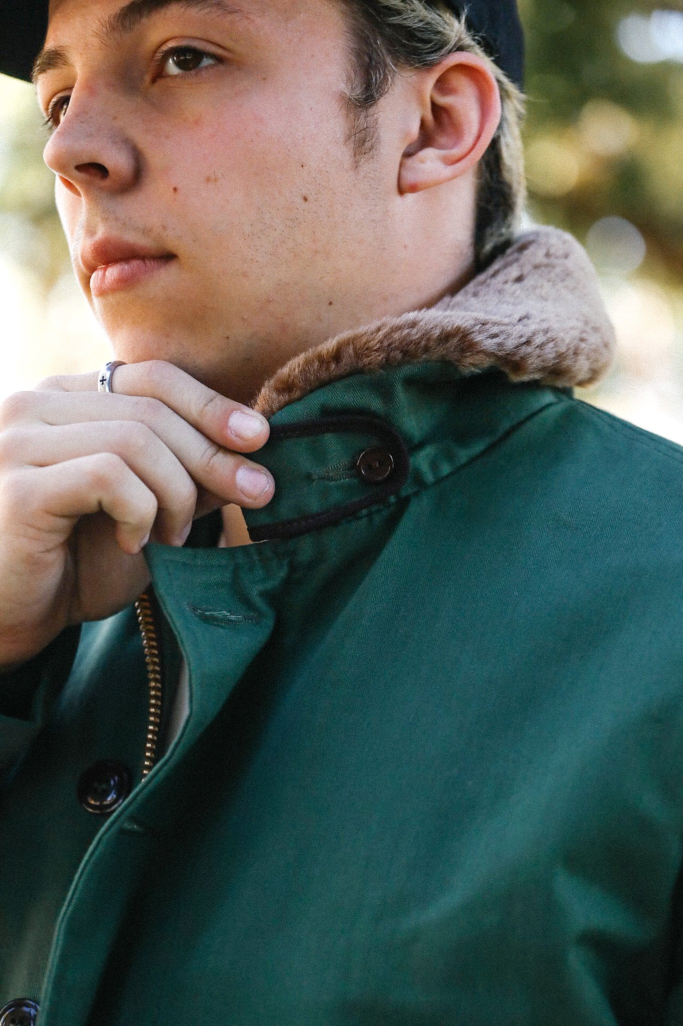 Close-up of a man adjusting a green jacket with a brown fur collar in natural light
