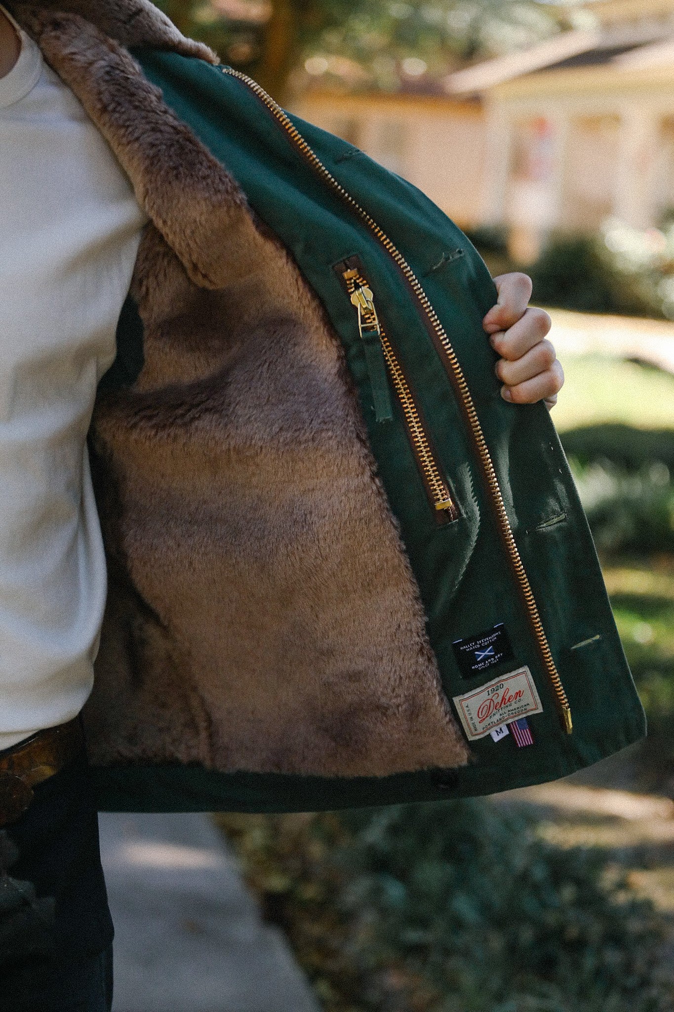 Close-up of a green jacket with soft brown fur lining and gold zipper, held open by person outdoors