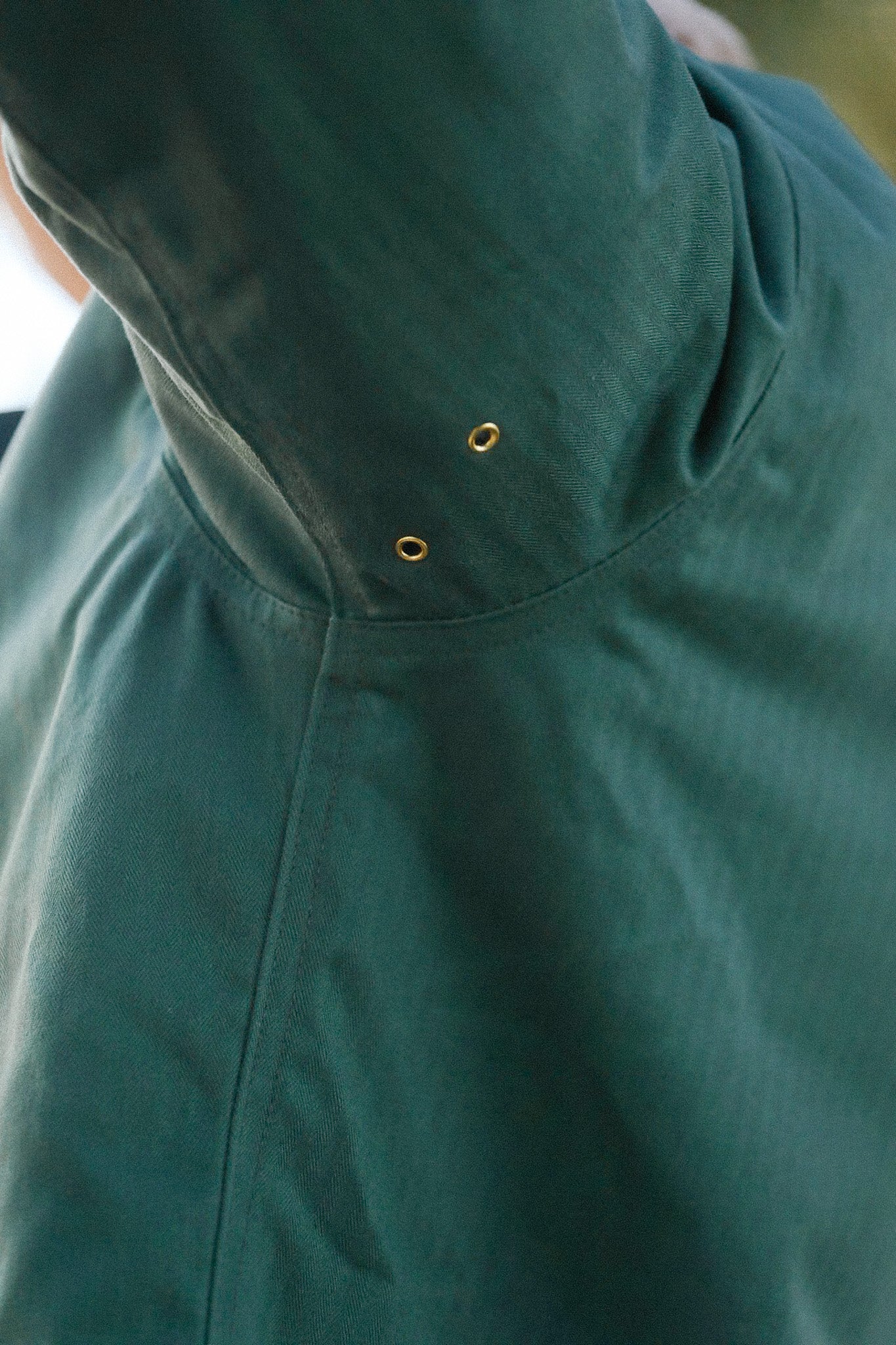 Close-up of green hooded jacket with brass eyelets showcasing durable fabric detail