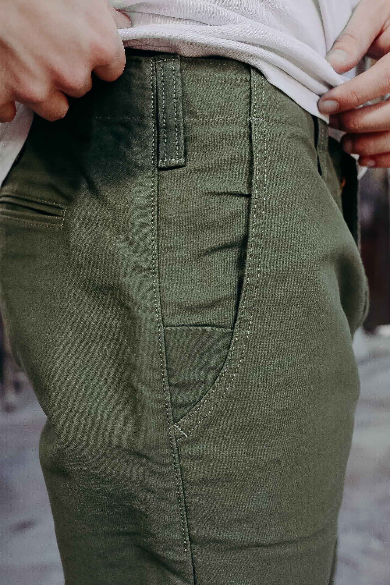 Close-up of olive green work pants pocket and belt loops with detailed stitching