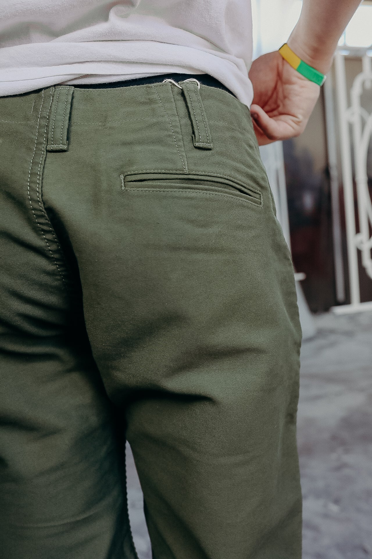 Close-up of person wearing olive green pants with detailed back pocket stitching and belt loops
