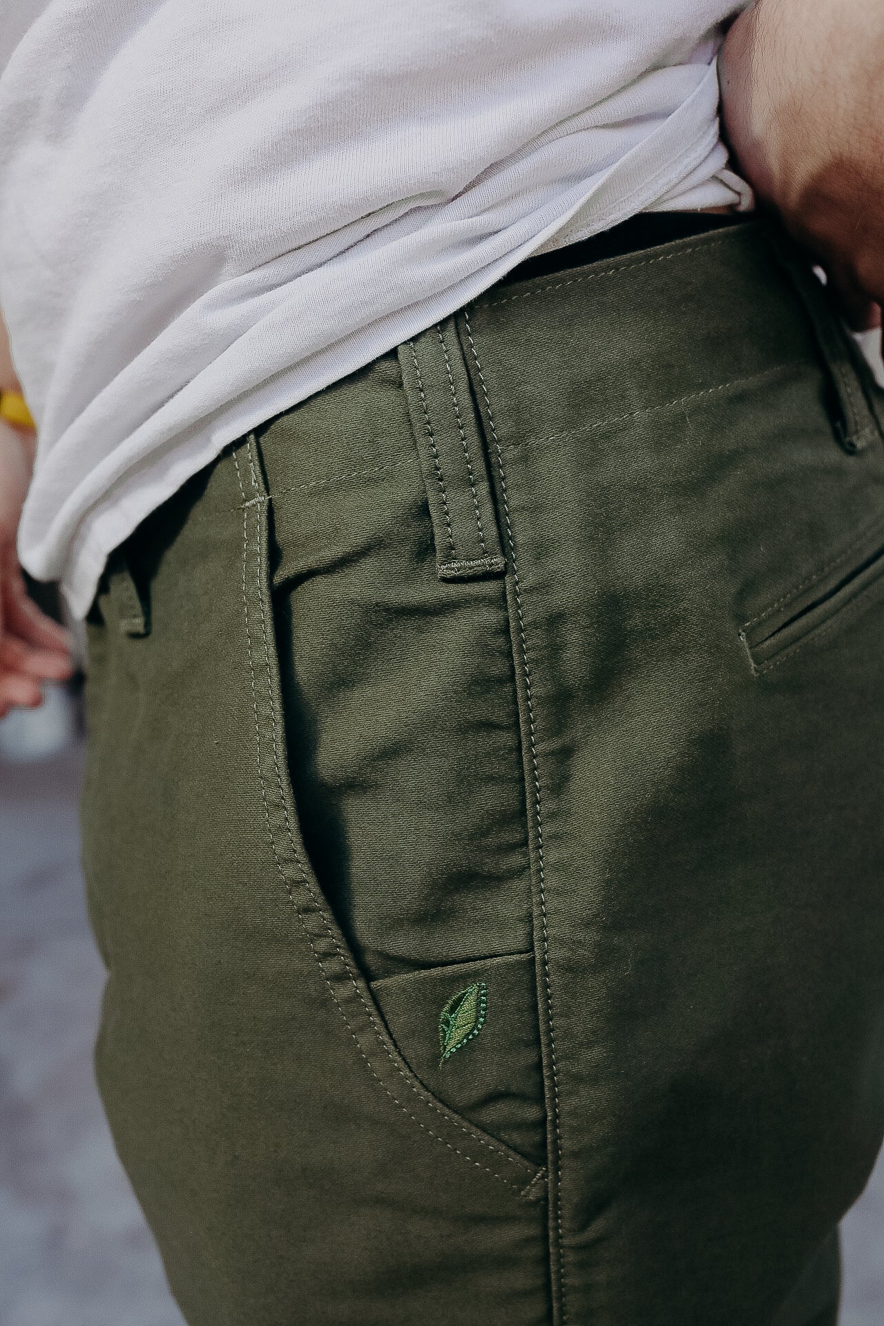 Close-up of olive green pants pocket with stitched leaf logo and white t-shirt tucked in