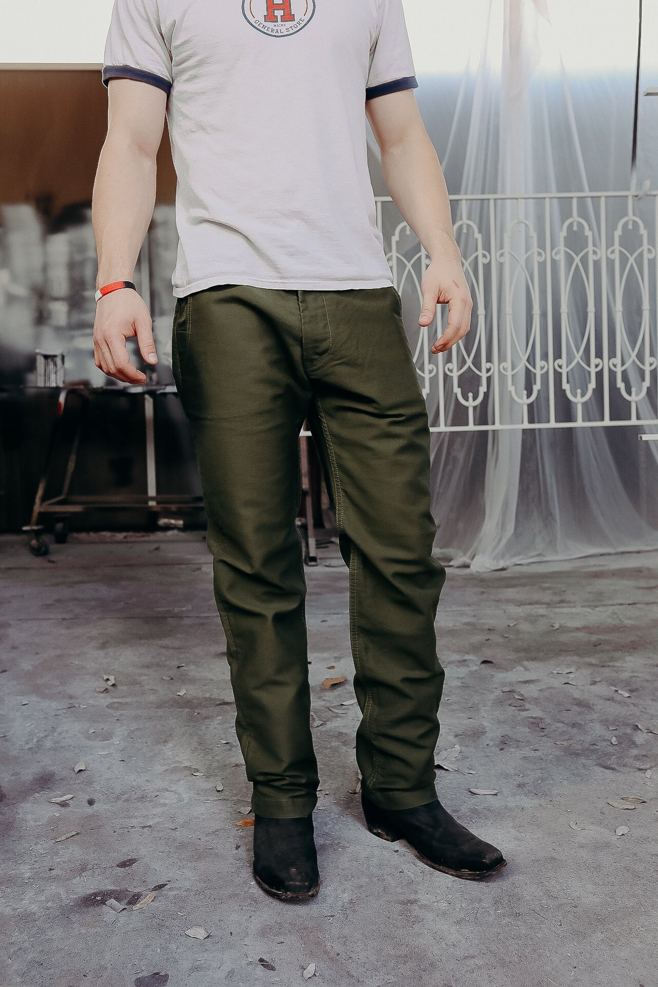 Man wearing green work pants and black boots standing in a rustic industrial setting